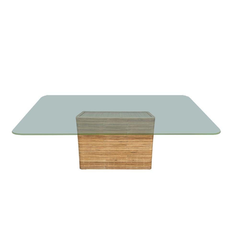 Franco Albini-inspired pedestal dining table features a striking stacked stick reed rattan base and natural rice mat top with a rectangle glass top. The rattan base offers a natural, earthy aesthetic with brass nail heads perfectly complementing the