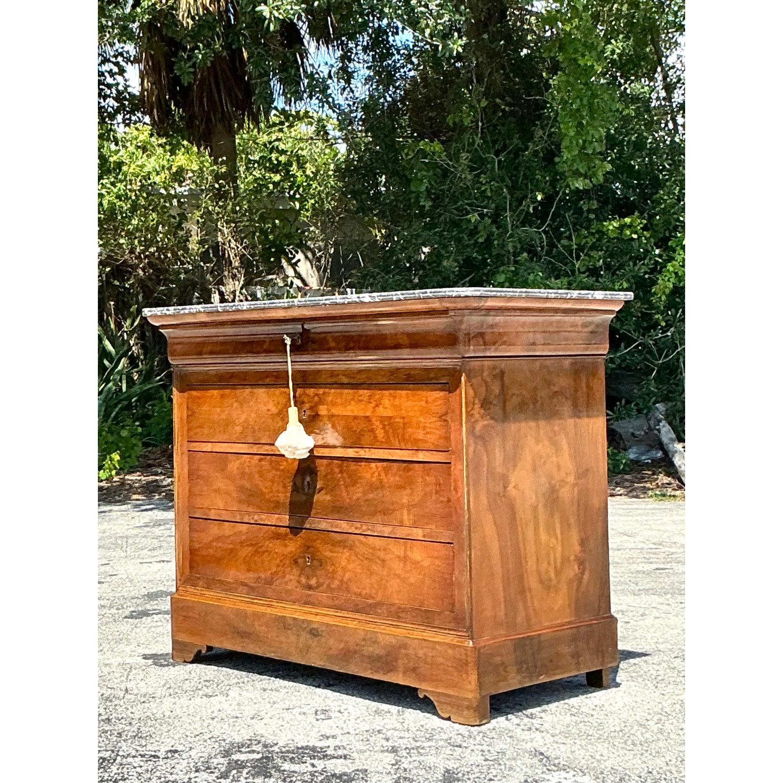 Fai un salto indietro nel tempo con questa squisita commode Louis Philippe del XIX secolo, testimonianza di un'eleganza francese senza tempo. Con una bella e resistente lastra di marmo grigio, questa cassettiera antica presenta le linee pulite