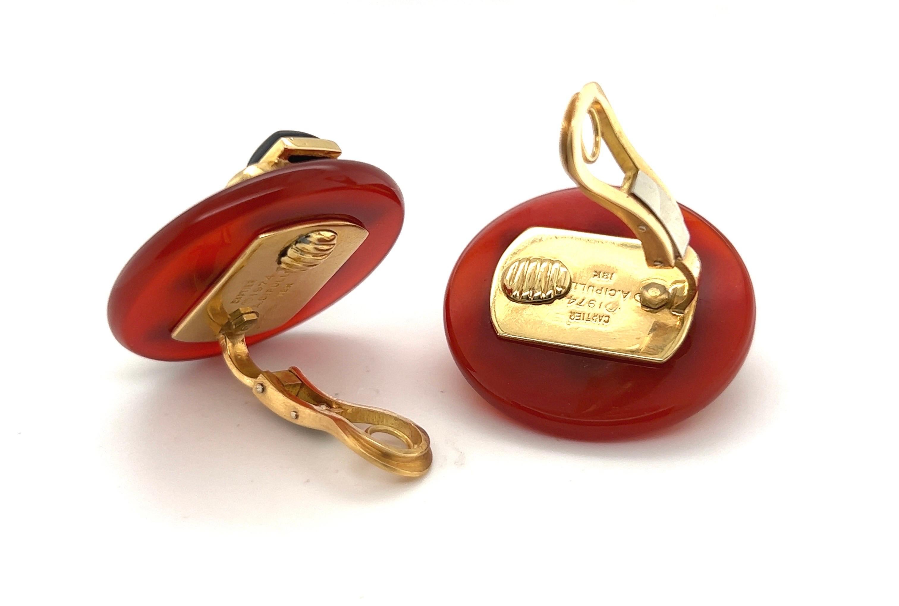 Iconic 18 karat gold, carnelian and onyx earrings designed by Aldo Cipullo for Cartier in 1974.
Geometrically designed ear clips each consisting of a deep red carnelian disc decorated with a trio of onyx sugarloaf cabochons set in yellow gold. The