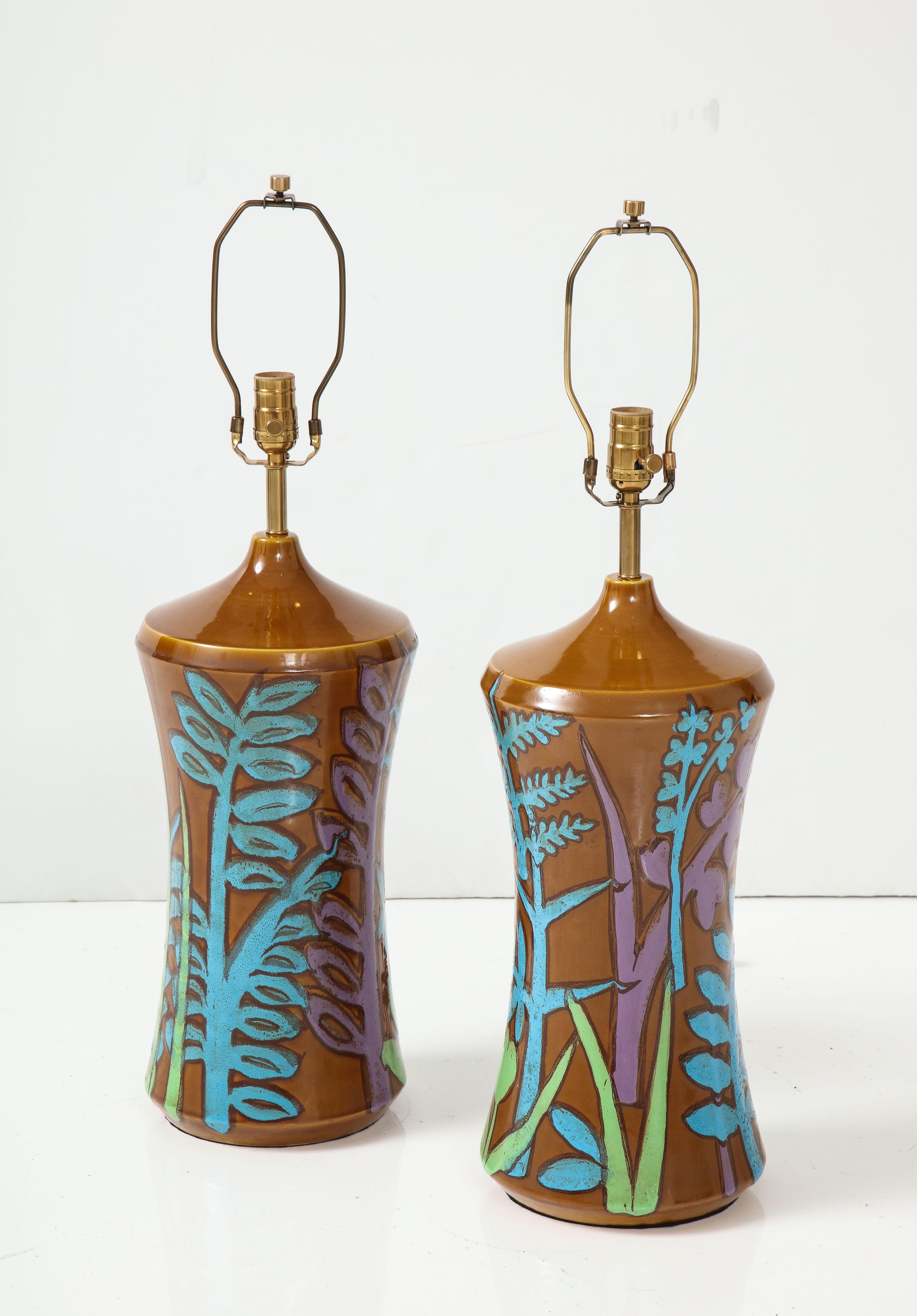 Pair of Italian hand decorated ceramic lamps feauring a light brown background and exhuberant stylized fauna and flowers in light blue, lilac, and celadon. Rewired for use in the USA with new brass sockets and silk cords. 100W max