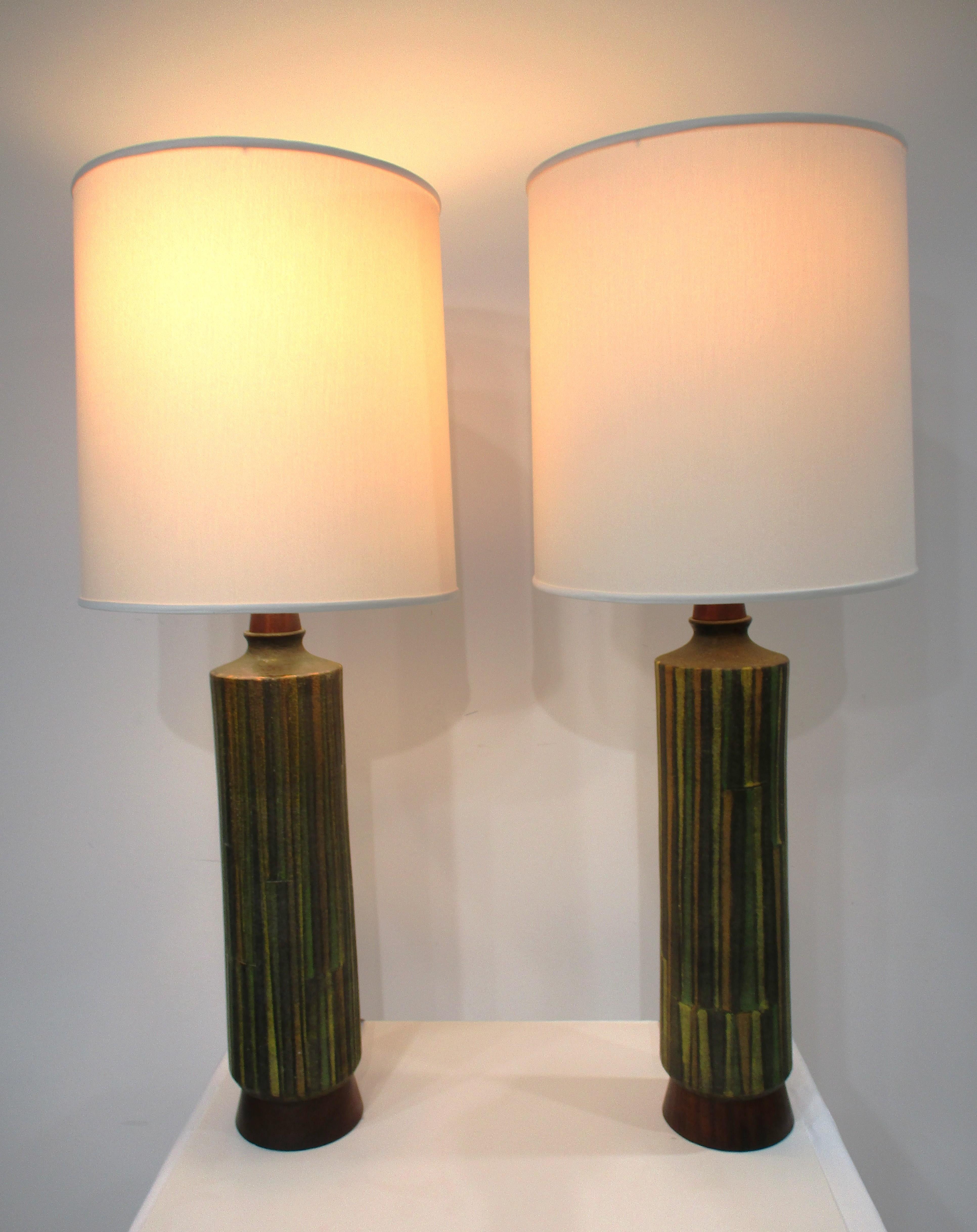 Un par de lámparas de sobremesa de cerámica Aldo Bitossi de mayor altura, hechas a mano, con base de nogal oscuro y pie con tonos verdes, tostados y amarillos oscuros, medios y claros, con diseños impresos en el cuerpo. Fabricada por Raymor de su