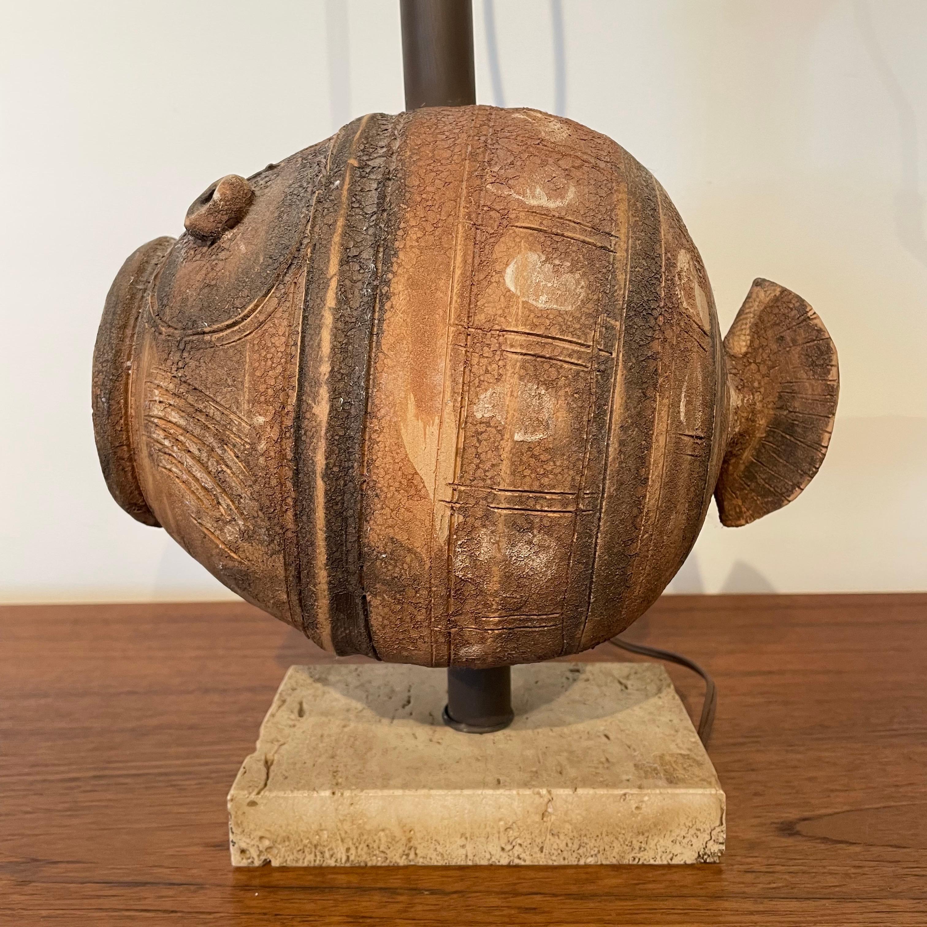 Lámpara de peces de cerámica esgrafiada sin esmaltar de mediados de siglo, diseñada por Aldo Londi para Bitossi. La figura del pez está montada sobre una base rústica de travertino. El enchufe conserva la etiqueta original de Raymor. El cableado