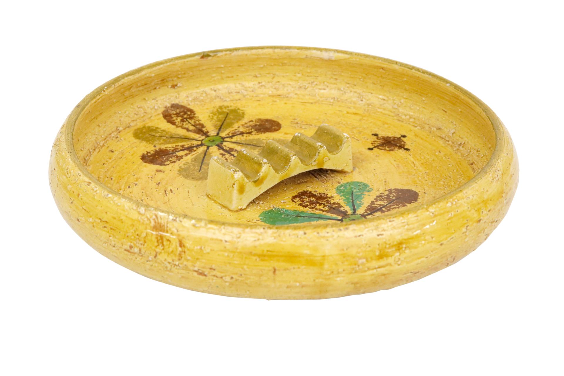 A 1950’s Aldo Londi for Bitossi Italian ceramic ashtray. Decorated with atomic style flowers in brown, teal and olive on a mustard yellow background. At the center is a raised cigarette holder. Rosenthal Netter label can be seen underneath.