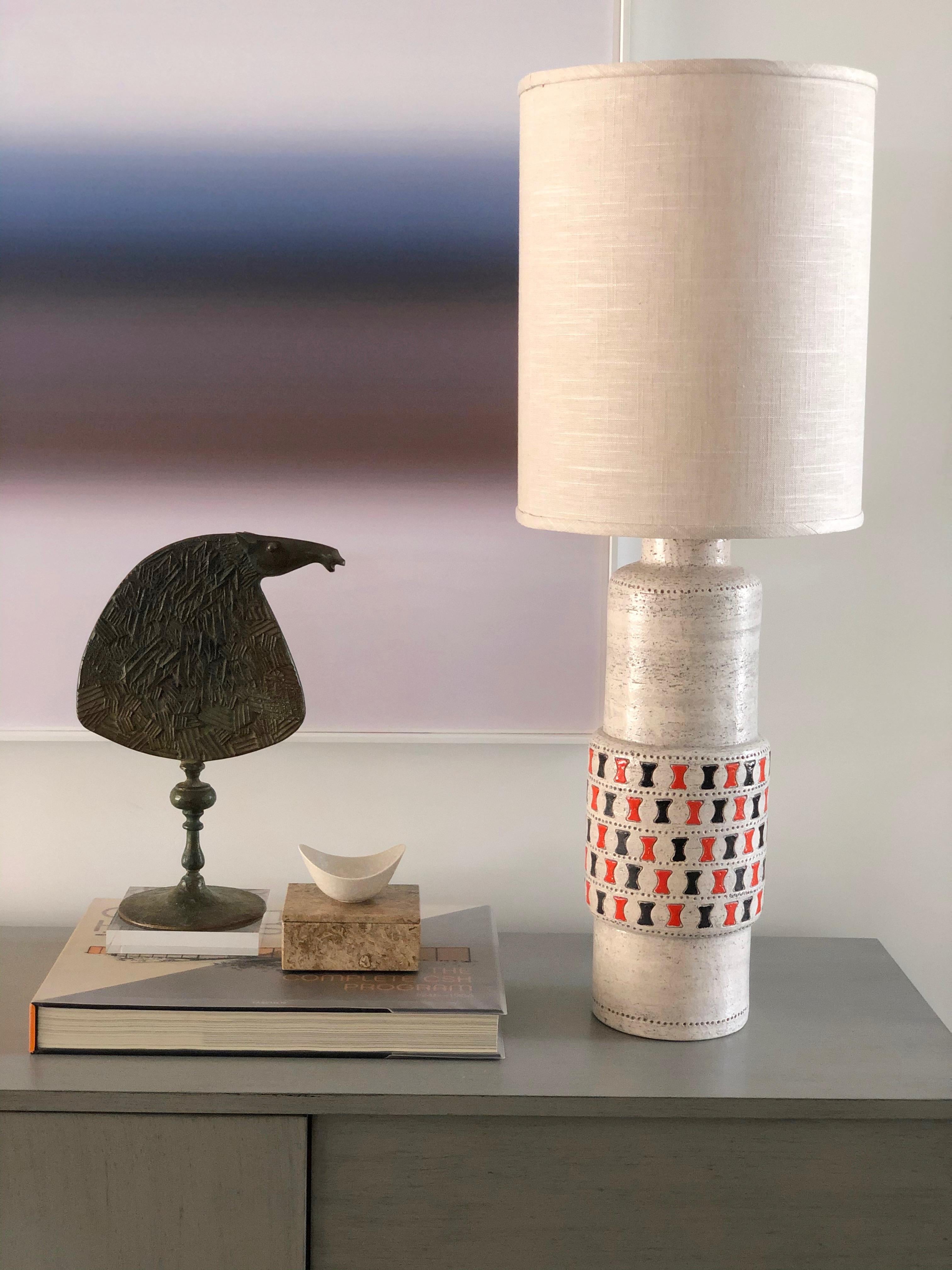 A vintage circa 1960s ceramic table lamp by Aldo Londi for Bitossi Ceramics. The lamp body is a greyish white with the 'denti' pattern in orange and black. The lamp has a new shade and is wired for use in the US. The shade measures 15