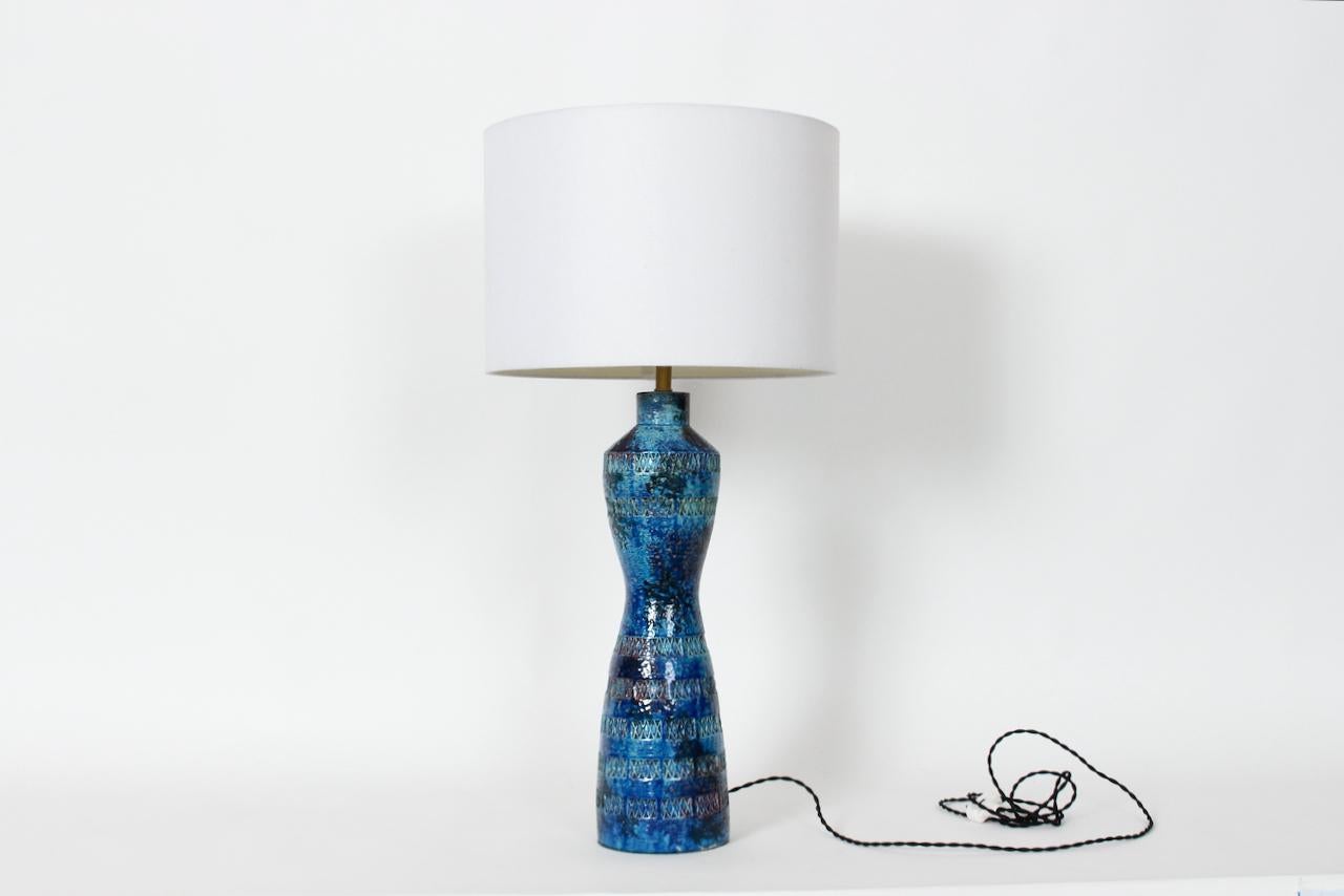 Italian Mid Century Aldo Londi for Bitossi Incised Blue Glazed Table Lamp. Featuring a handcrafted hourglass pottery form, horizontal imprinted crossed accents, varied Blue tones, Deep Blue waist and sprinkling of Red. 22.5 H to top of socket. 18H