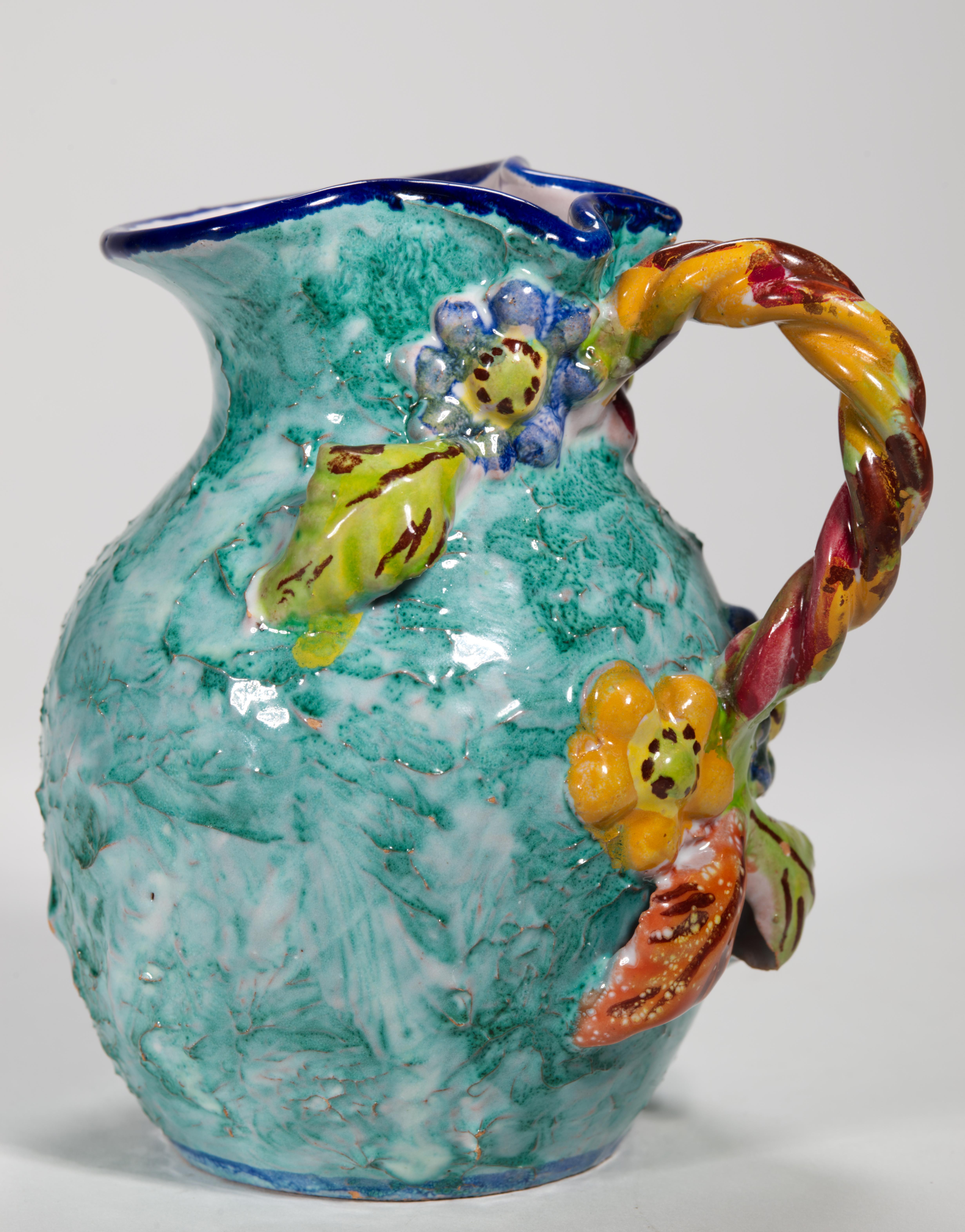 Set of vintage majolica bud ewer vase and dresser box with lid features highly textured surfaces with complex teal glaze; the pieces are decorated with abstract flowers and leaves in relief. On the vase the flowers are hand-painted red, orange, and