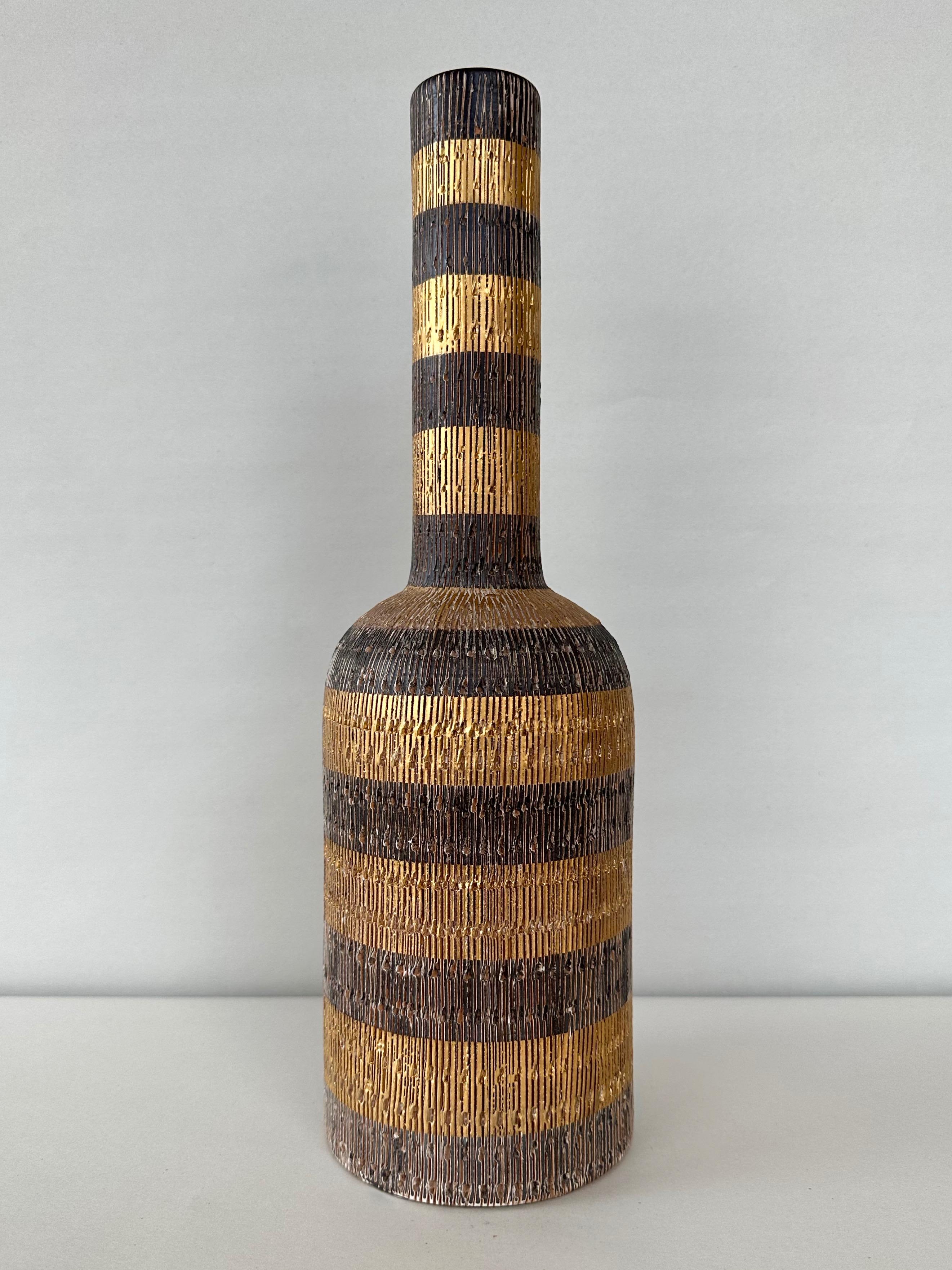 An uncommon 1950s Italian tall bottle-shaped Seta vase by Aldo Londi for Bitossi and retailed by Raymor.

Very handsome alternating bands of satin metallic gold and matte dark coffee glaze over a hand-incised brown pottery body. Bands are notable
