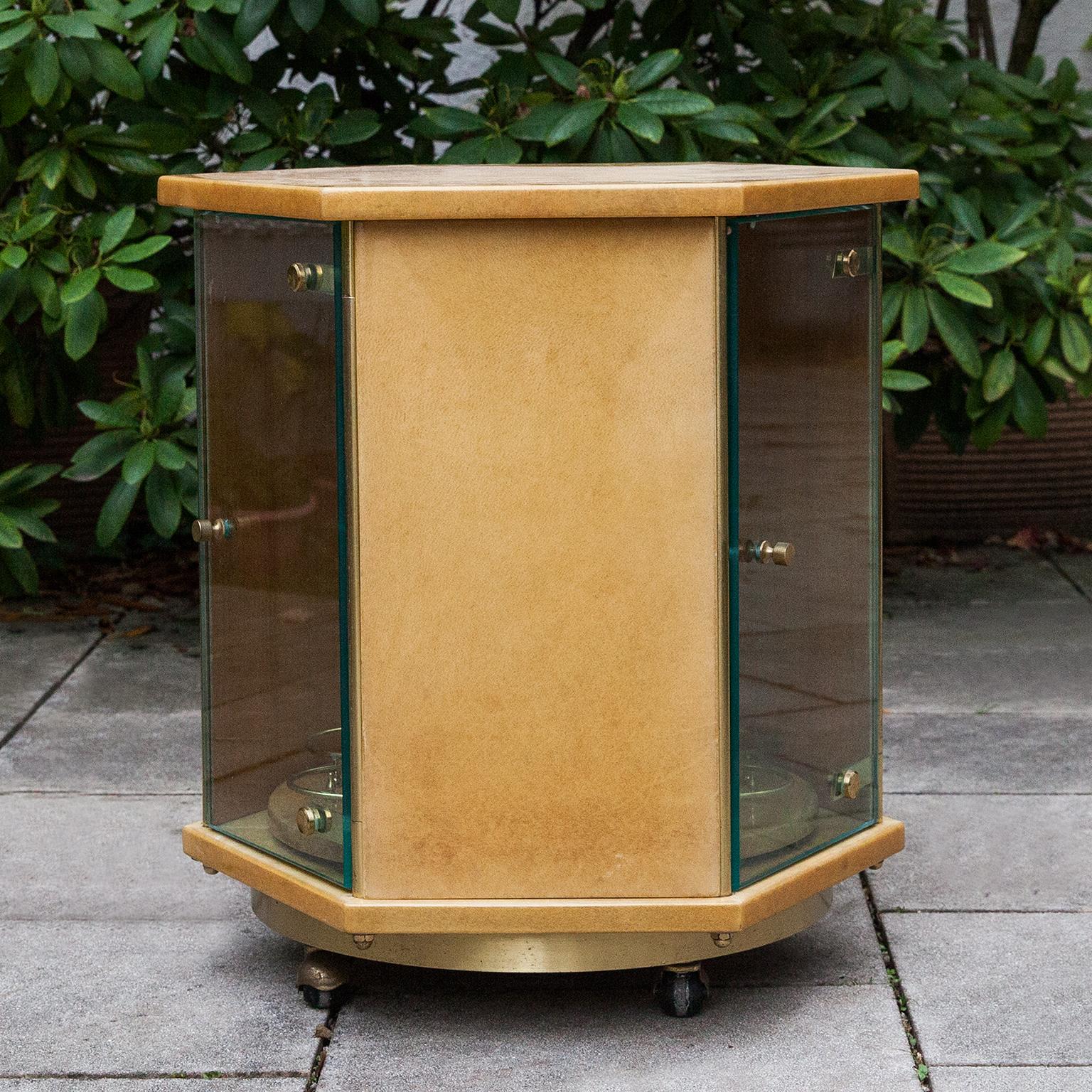 Elegant Aldo Tura bar cart on brass rolls in hexagonal shape with three glass doors and a turnable bottle holder inside.

This particular bar cart was executed, circa 1970 and is in excellent condition. Along with artists like Piero Fornasetti and