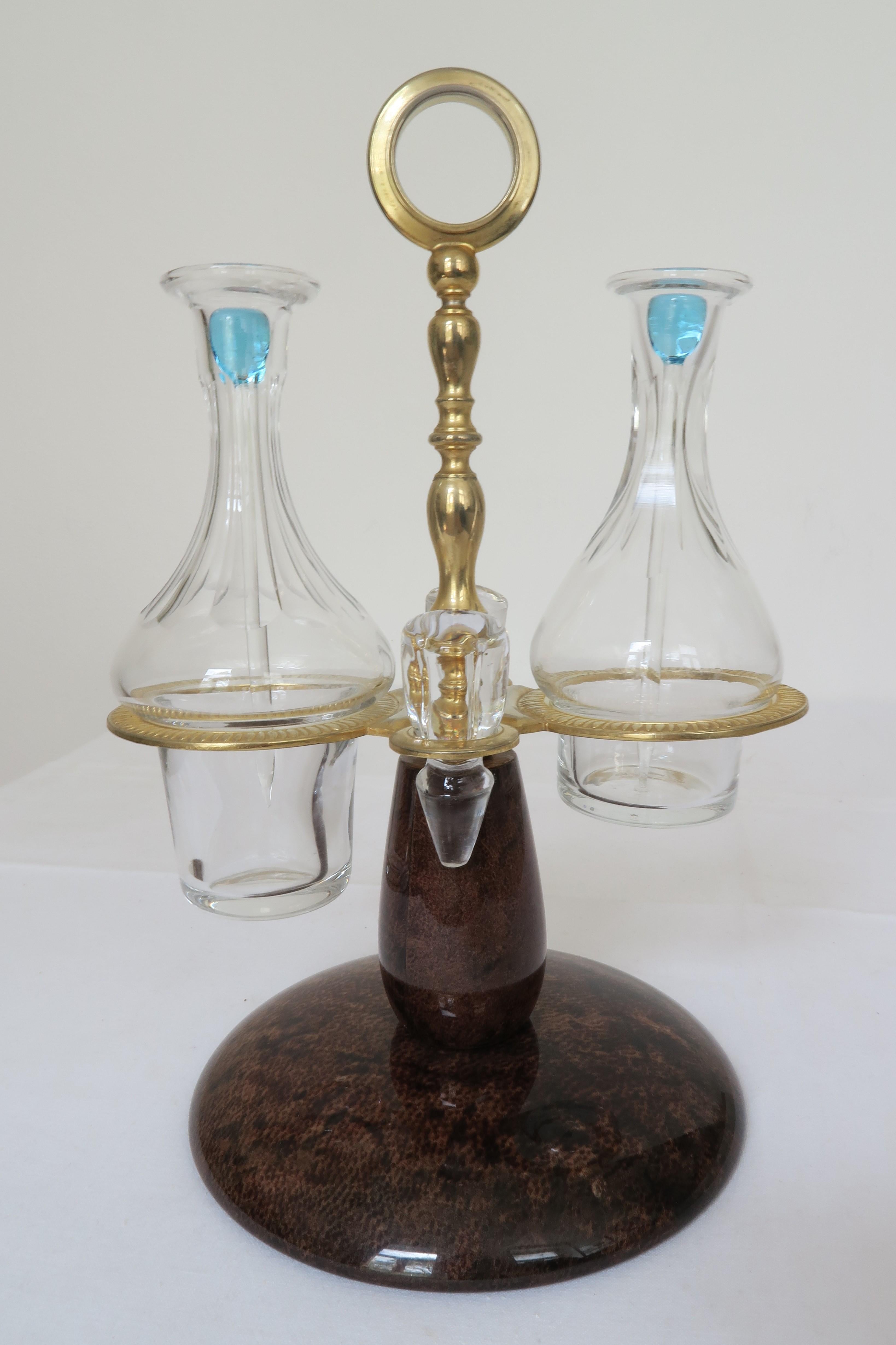 For sale is a beautiful and unique cruet stand by Italian creator Aldo Tura. It has a varnished brown leather foot with glowing brass hardware and cut glass pitchers for oil and vinegar. The pitchers can be closed with cut glass stoppers or can be