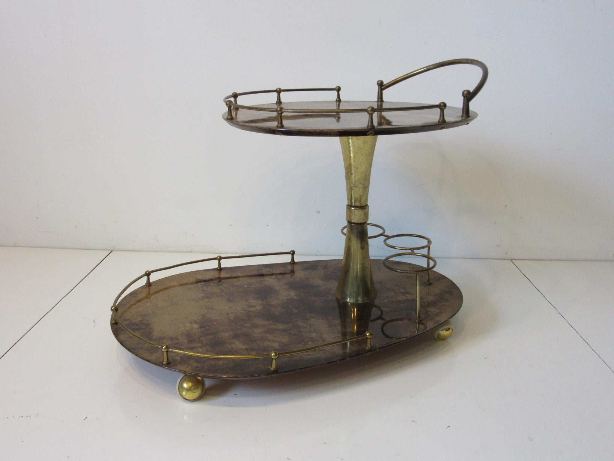 A goatskin covered double tiered rolling bar cart with brass wheels, brass rails, handle and three ring bottle holder. The top part of the cart is held up by a brass tulip styled pedestal, well crafted and designed by Aldo Tura who used goatskin to