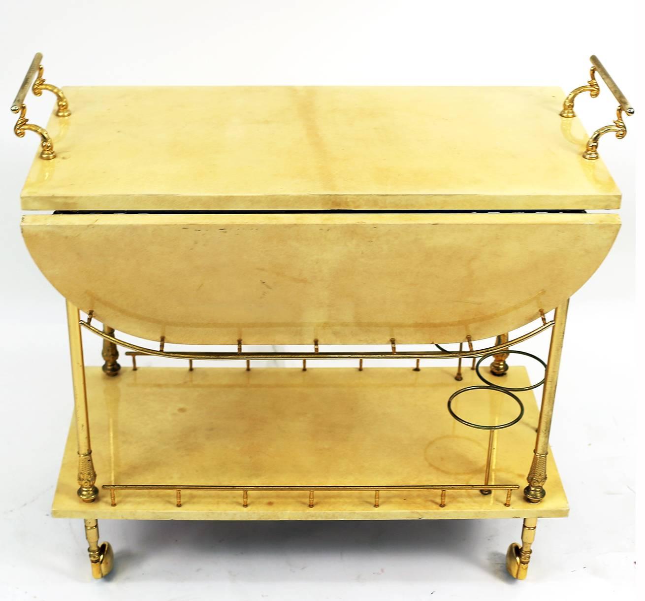 A beautiful ecru colored Aldo Tura lacquered goatskin two level bar cart trolley with drop down leaves and brass detailing. Excellent condition. 

Overall dimensions of cart with drop leaves extended are 31 inches in length, 31 inches in depth and