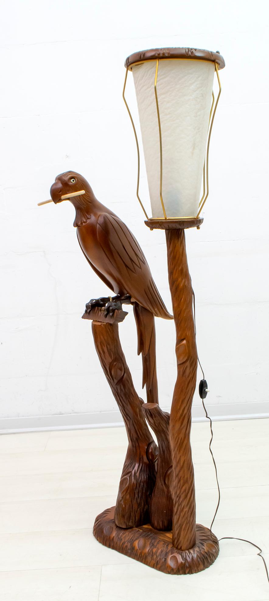 Ce lampadaire en bois sculpté a été conçu par Aldo Tura ; il peut être daté des années 1950. La sculpture en bois représente un perroquet, la lanterne avec des supports en laiton et en peau de chèvre. Cette lampe est en excellent état d'origine.