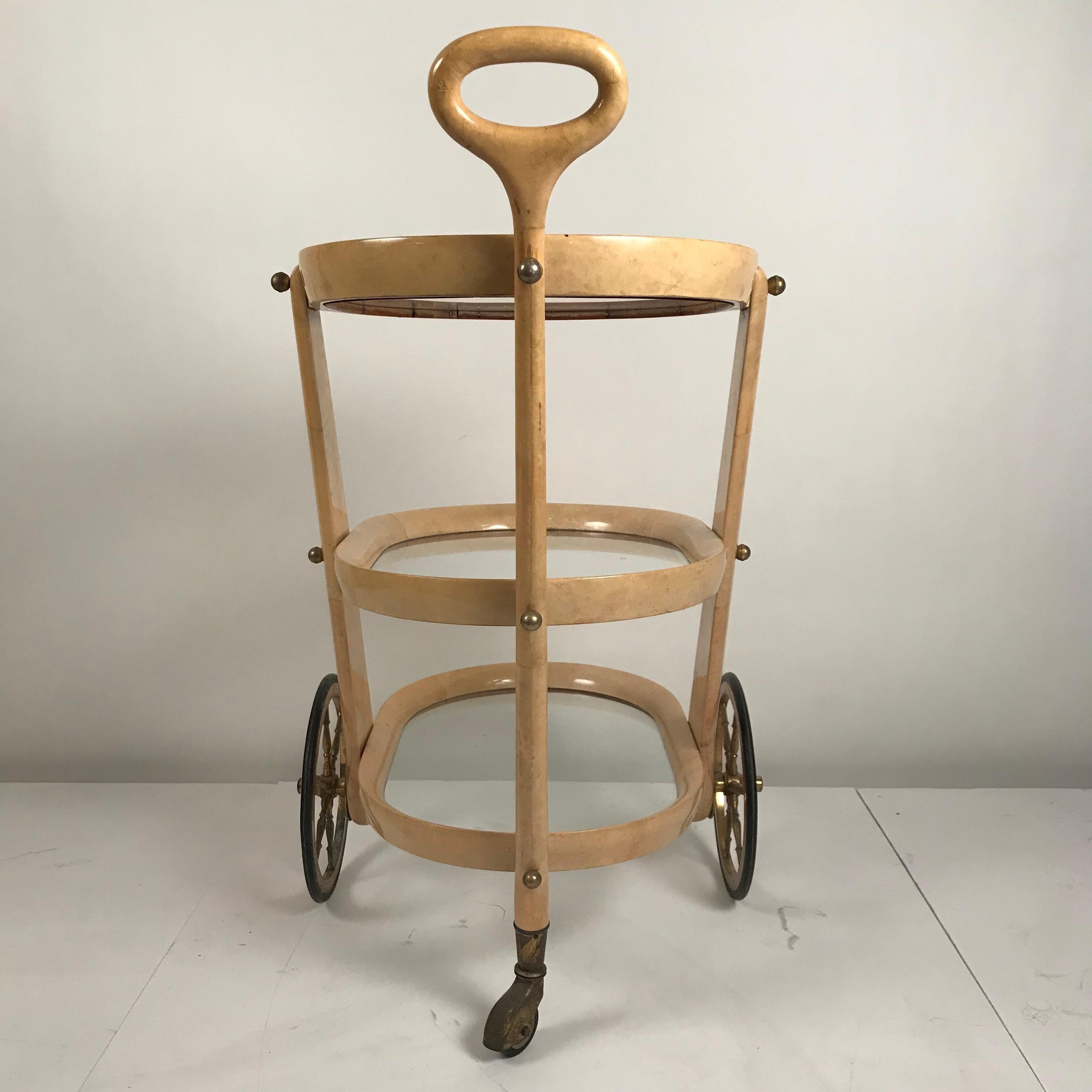 Elegant and rare bar cart by Aldo Tura / Milano. The wooden structure is covered with clear coated parchment in it's natural color. The metal fittings and wheels are made in brass.
