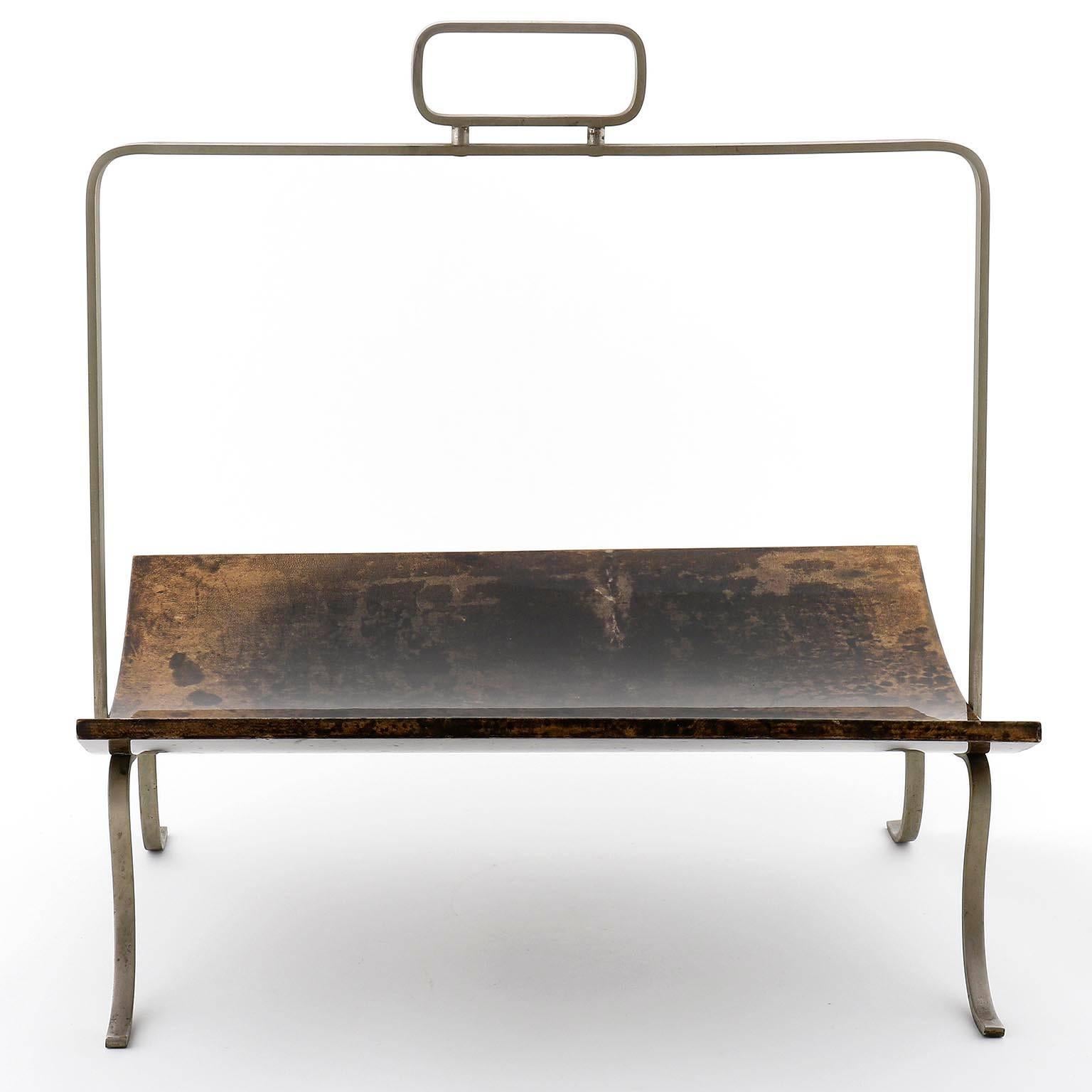 An Italian newspaper stand by Aldo Tura, manufactured in midcentury, circa 1970 (1960s-1970s).
The stand is made of natural aged nickel plated brass with lovely patina.
The shelf is made of bent wood, covered with brown and black goatskin and