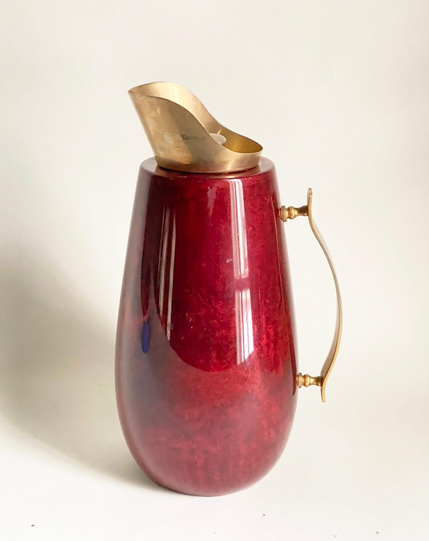 Voici un très beau pichet ou carafe du milieu du siècle dernier du designer italien Aldo Tura. Ce modèle est présenté dans un magnifique parchemin rouge laqué avec des accents en laiton. Cet exemplaire est en très bon état - le revêtement en verre