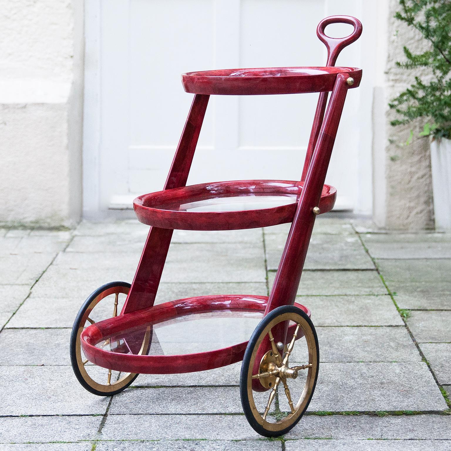 Wonderful bar cart of Aldo Tura in lacquered red goatskin with three glass shelves and brass wheels. This serving cart was executed, circa 1960 in a red parchment. Along with artists like Piero Fornasetti and Carlo Bugatti, Aldo Tura (1909-1963)