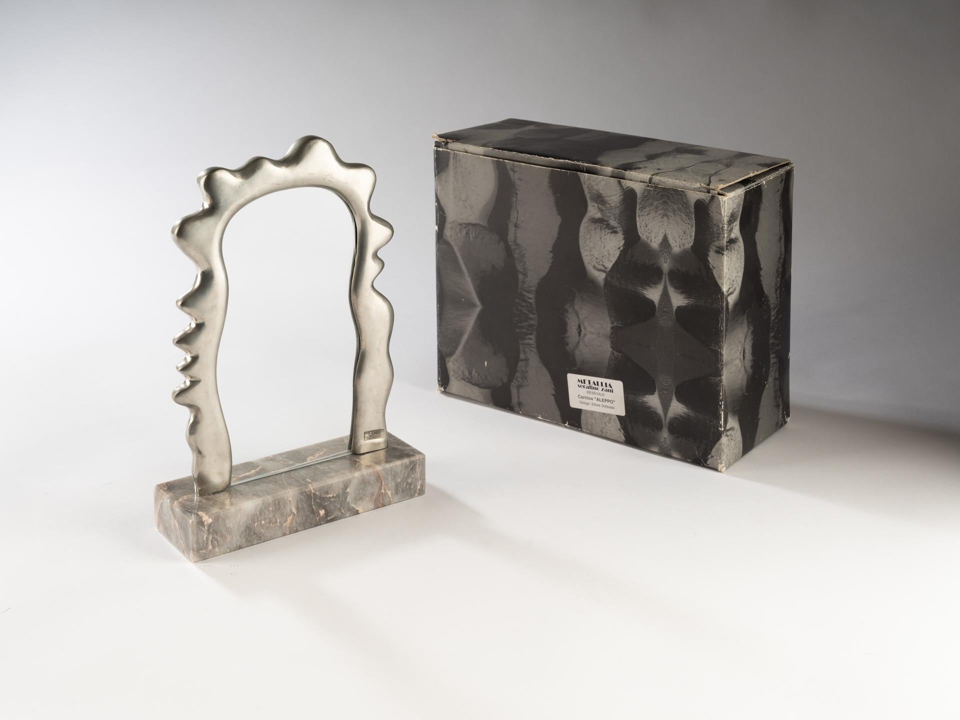 The Aleppo Frame designed by Ettore Sottsass for Metallia Serafino Zani in 1999 is made of Pewter, Glass and Grey Marble. The shape of this small frame was most likely inspired by the Ultrafragola Mirror, that Sottsass designed almost 30 years
