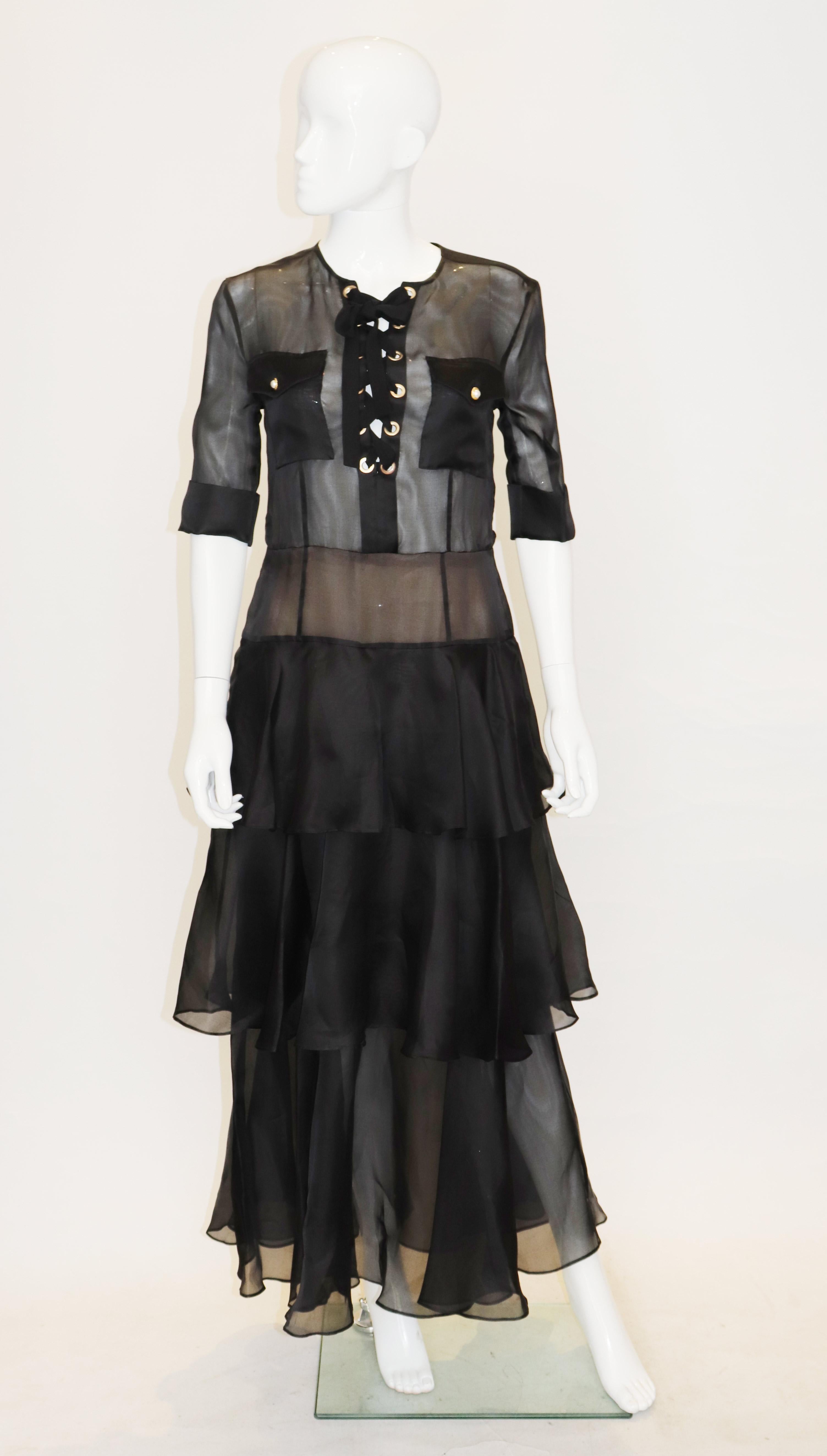 A head turning and chic gown in black silk by Alessandra Rich. The gown is collarless and has two breast pockets , short sleeves with turn up cuffs and a central back zip. It has a tiered skirt.