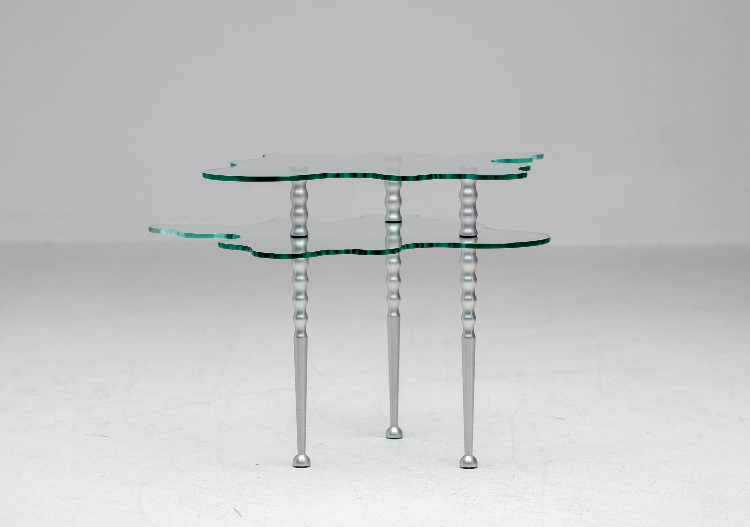 Alessandro Mendini designed the Papio table from his Nuova Alchimia collection in 1985.
This elegant table made of aluminum and crystal glass is very versatile, it offers endless compositions because the top glass top is not connected to the base.