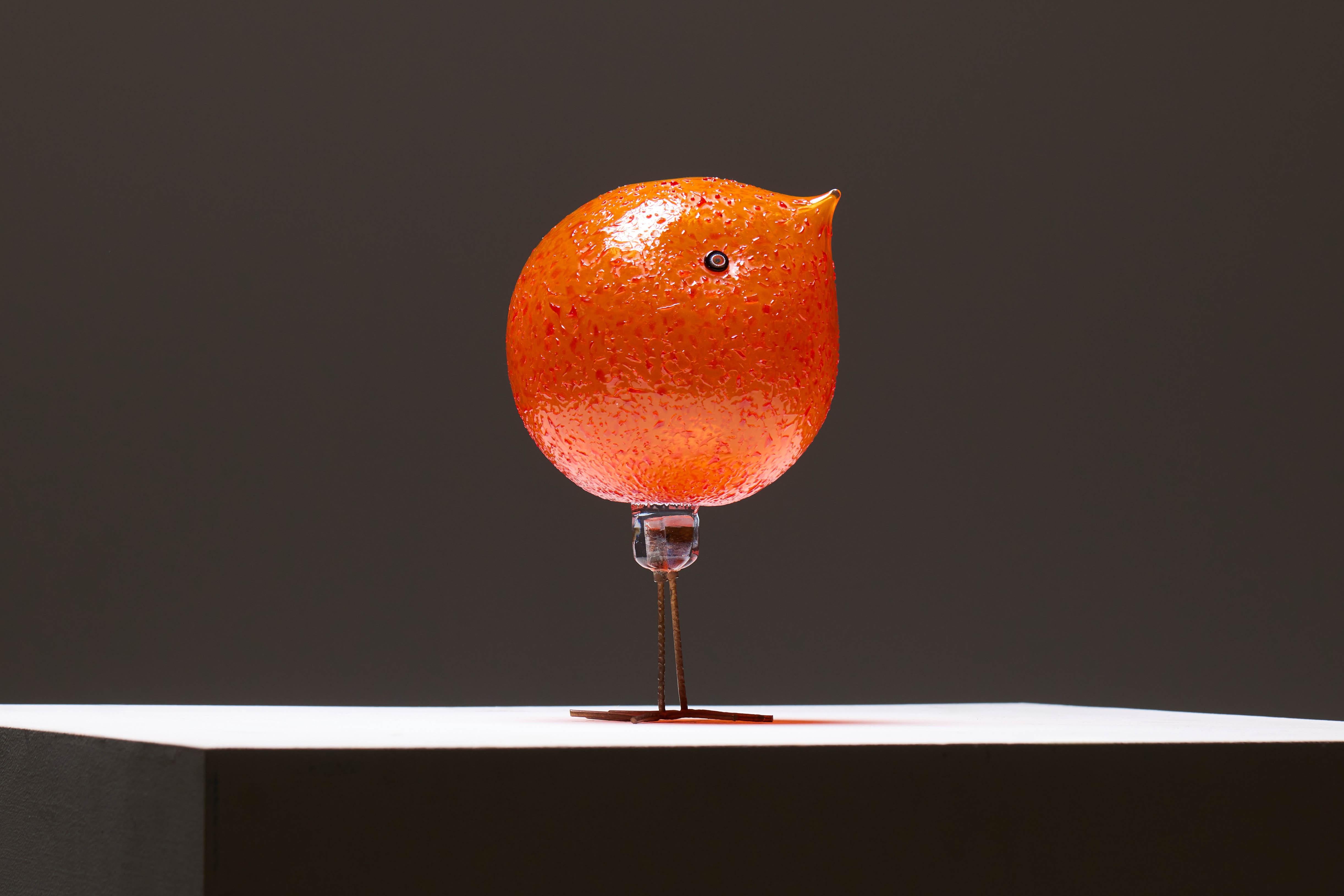 Questo uccello Pulcino è stato disegnato da Alessandro Pianon per Vistosi nel 1962. Soffiato a mano in vetro di Murano rosso arancio brillante e montato su gambe in rame martellato, è uno degli uccelli scultorei che insieme formano la serie Pulcino.