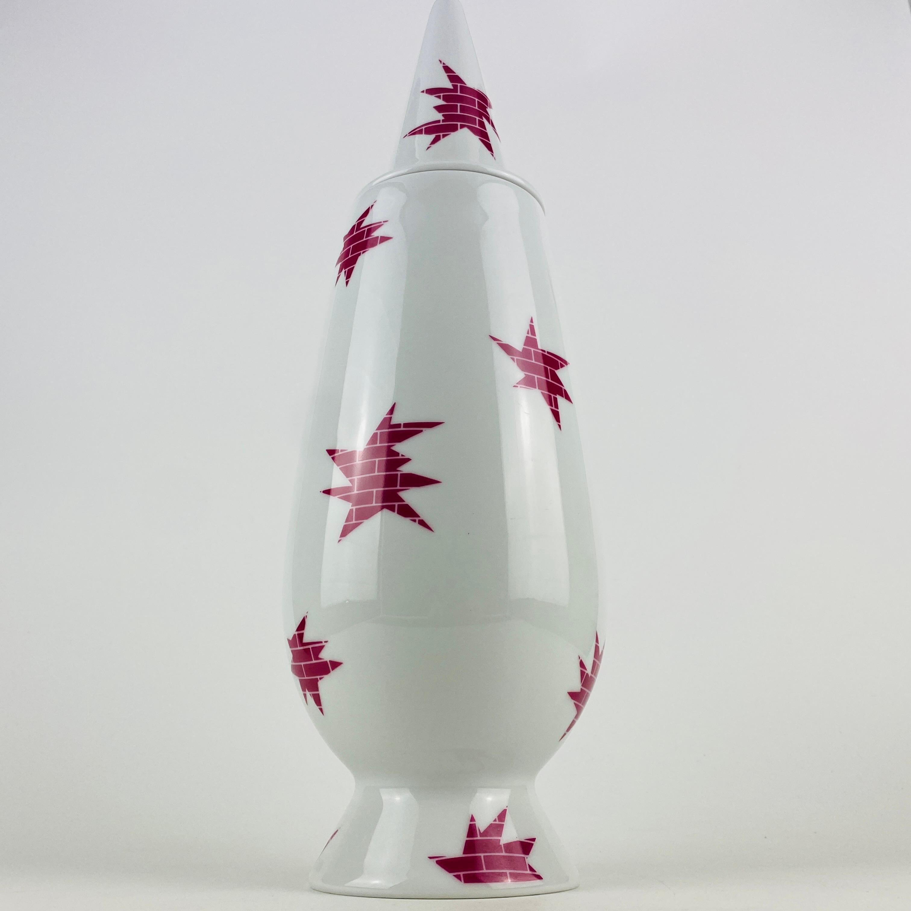 Questo vaso Tendentse Alessi con coperchio fa parte della serie limitata di 10.000 pezzi 100% make-up. Questa serie comprende 100 vasi diversi e 100 designer/decoratori diversi. 

Questo vaso in particolare è stato disegnato da Alessandro Mendini