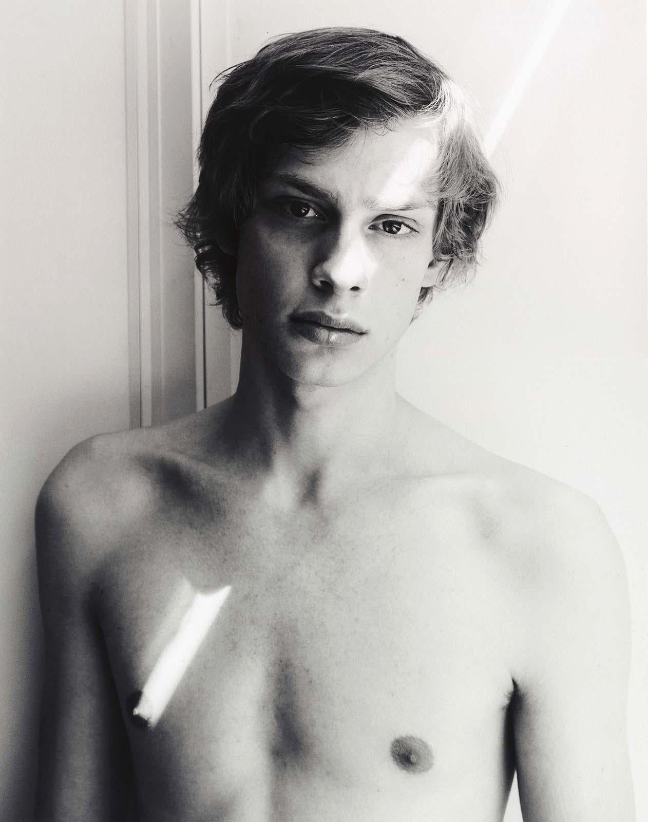 Alex Avgud Figurative Photograph – Jay and a Ray of Sun (the sun slants across young man's body from eye to nipple)