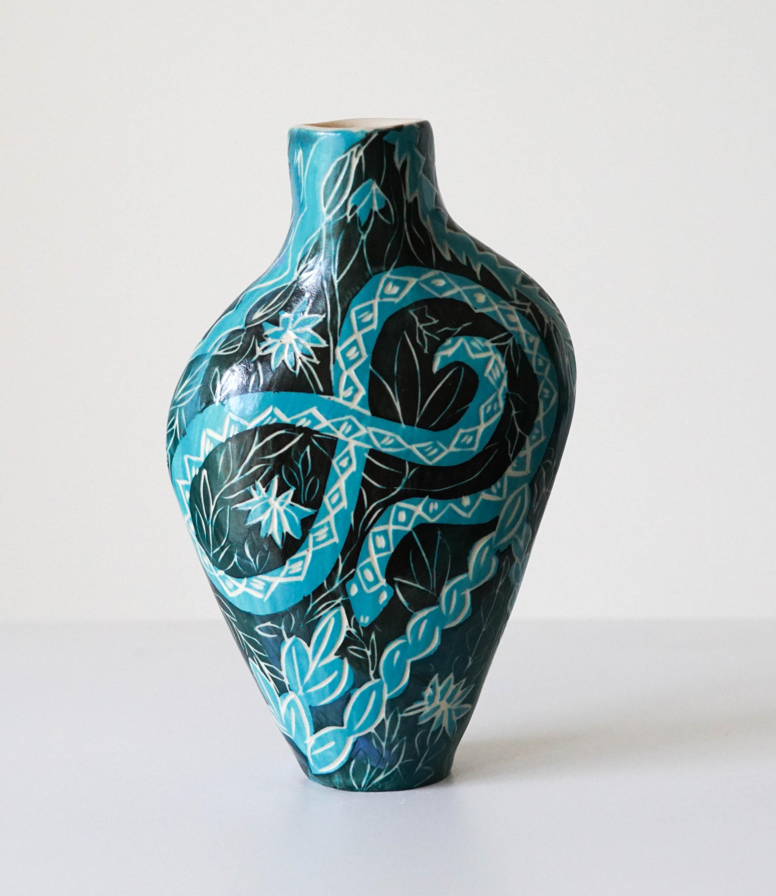 Ce petit vase en céramique présente des couleurs vives et froides et des formes végétales, avec des serpents enroulés comme personnages centraux. L'esthétique de la jungle accentue les connotations denses du serpent en tant que symbole à travers