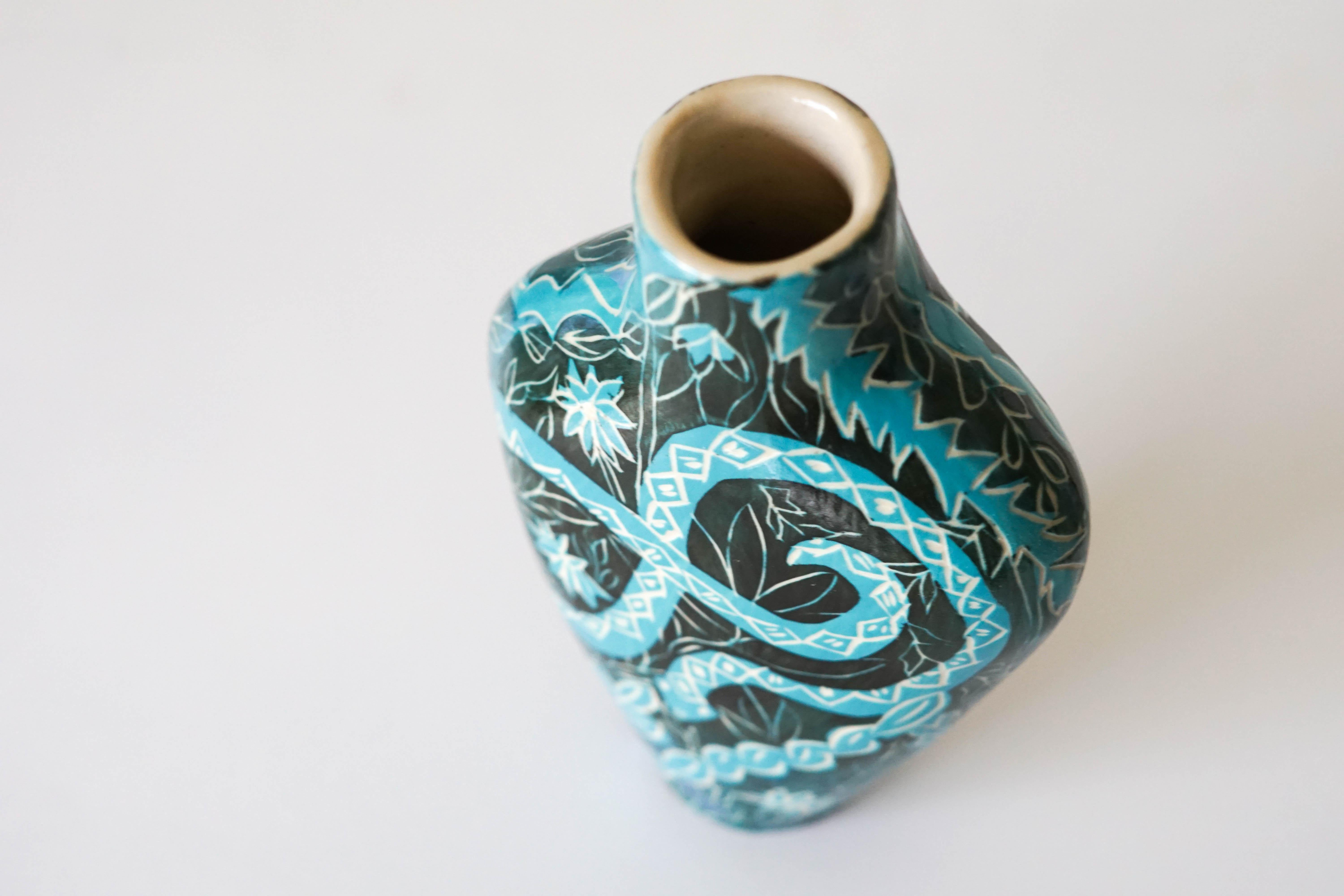 Charmante Schlangen
Keramikvase mit Unterglasur-Sgraffito-Details

Diese zierliche Keramikvase zeichnet sich durch helle, kühle Farben und Pflanzenformen aus, in deren Mittelpunkt sich Schlangen winden. Die Ästhetik des Dschungels unterstreicht die
