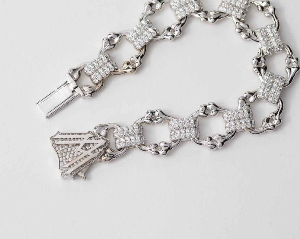 Il bracciale Crushed Bones di Alex Moss combina maglie a forma di osso non convenzionali con un tocco elegante. Queste maglie, realizzate in oro liscio con finitura lucida, sono collegate da due anelli impreziositi da diamanti naturali, creando un