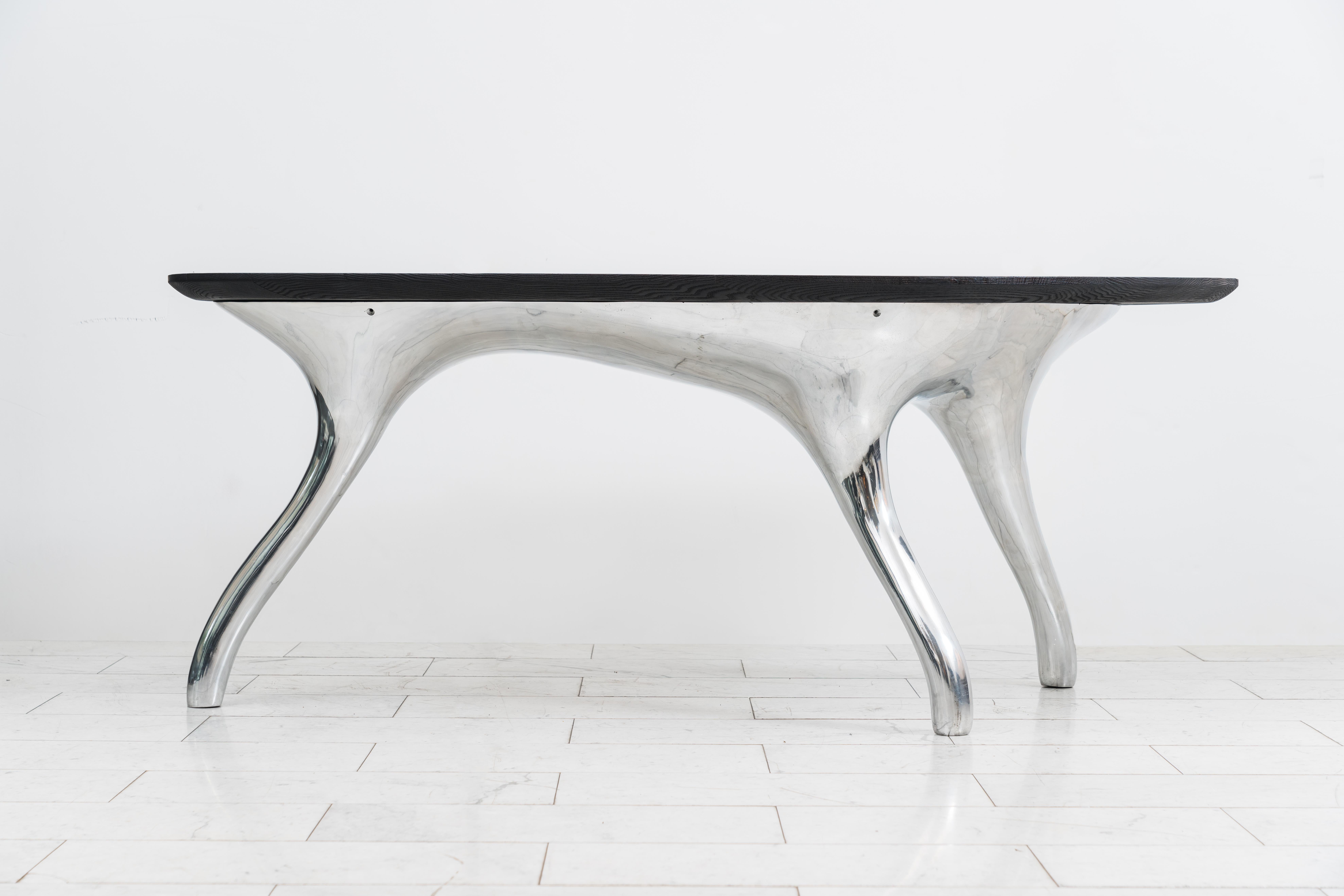 Alex Roskin’s Trois Jambes Dining Table rests on a sparkling tripod base of mirror-polished stainless steel, the asymmetric table top is shown with a wood top finished in the shou sugi ban method. Available by commission, the table can be customized