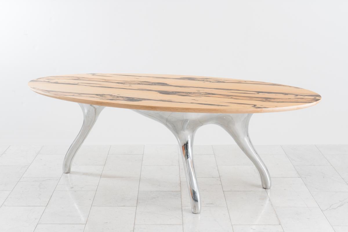 Alex Roskin’s dynamic white ebony dining table, titled Trois Jambes, rests on a polished aluminum tripod base. The pale straw color of the white ebony, with its dramatic black streaks, is bookmatched in an alternating pattern emphasizing the