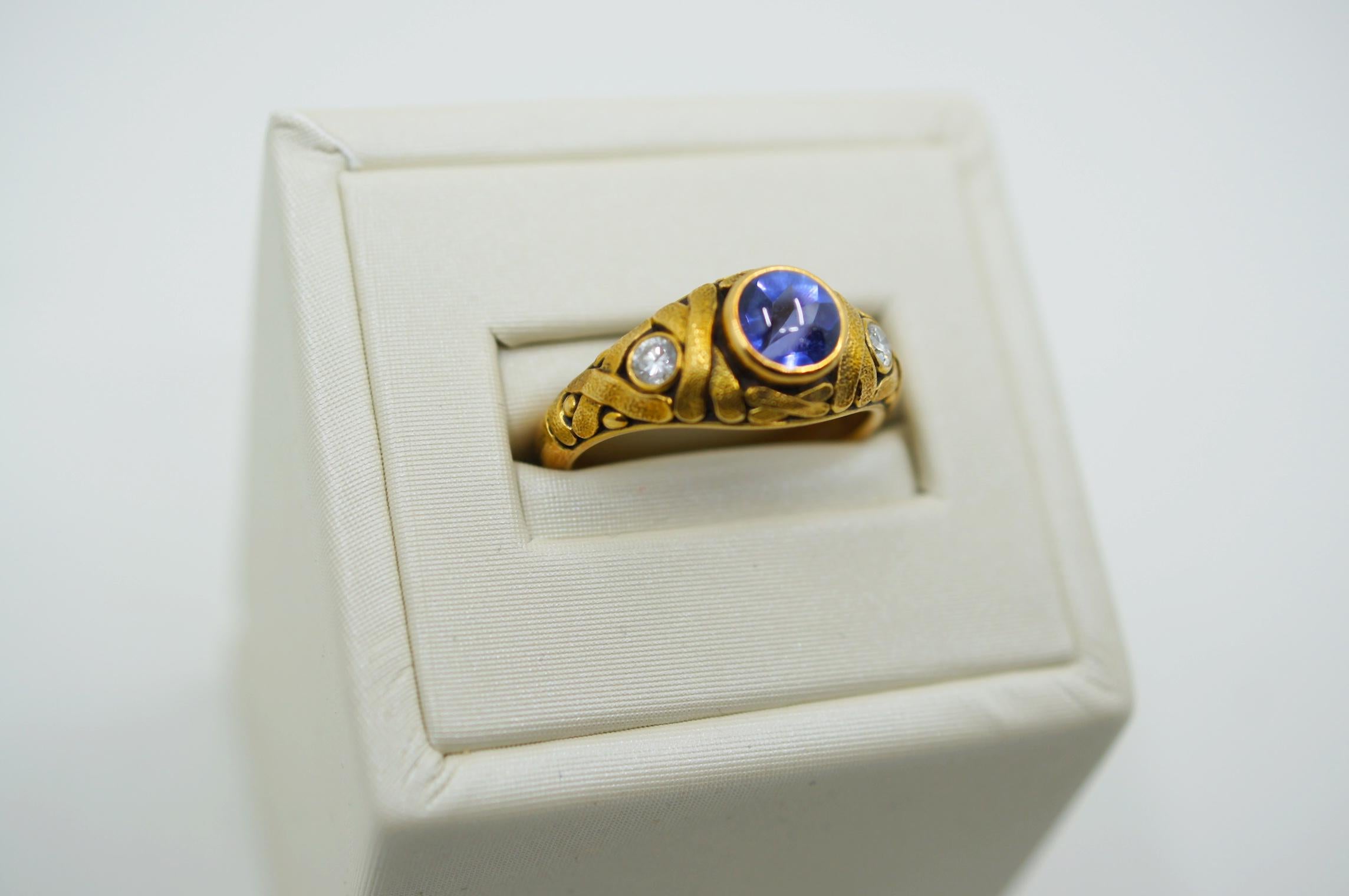 Alex Sepkus ring centering a gorgeous circular cabochon-cut tanzanite measuring approximately 6mm in diameter and 1.04 carats in a hand-engraved 18k yellow gold 'X' weave-patterned mounting with two single round-cut diamonds at either shoulder,