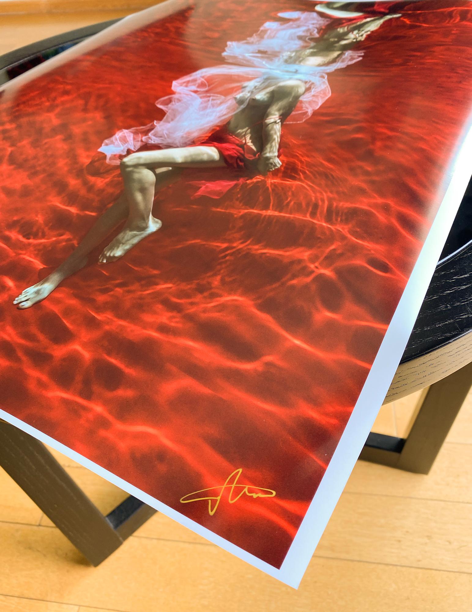 Ein Unterwasserfoto einer jungen Frau ohne Oberteil mit weißem Tüllschal, die ihren roten Rock auf leuchtend rotem Hintergrund auszieht. 

Original-Pigmentdruck in Galeriequalität auf Archivpapier, vom Künstler signiert.
Papierformat: 18