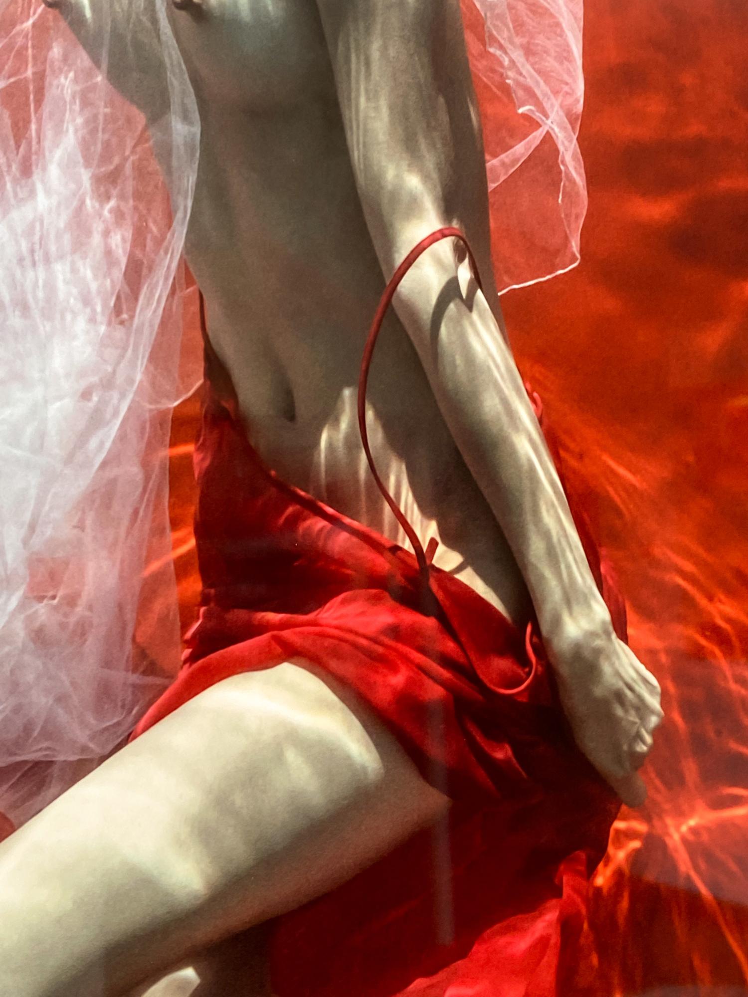 Ein Unterwasserfoto von einer jungen Frau mit weißem Tüllschal, die ihren roten Rock vor einem leuchtend roten Hintergrund auszieht. 

Original-Digitaldruck auf Aluminiumplatte, vom Künstler signiert.
Limitierte Auflage von 12 Stück, Druck Nr. 2
Das