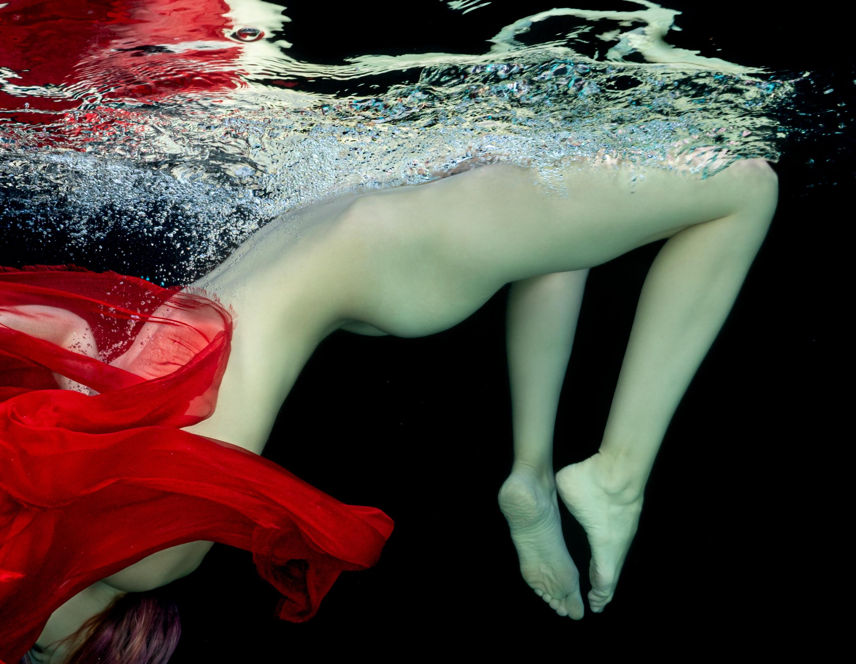 Unterwasseraufnahme einer jungen nackten Frau beim Tauchen in einem Pool. Ihr Gesicht ist mit einem roten Schal bedeckt. Ihr schöner nackter Körper und der rote Schal sehen frisch und lebendig aus  auf schwarzem Hintergrund.

Originalabzug in
