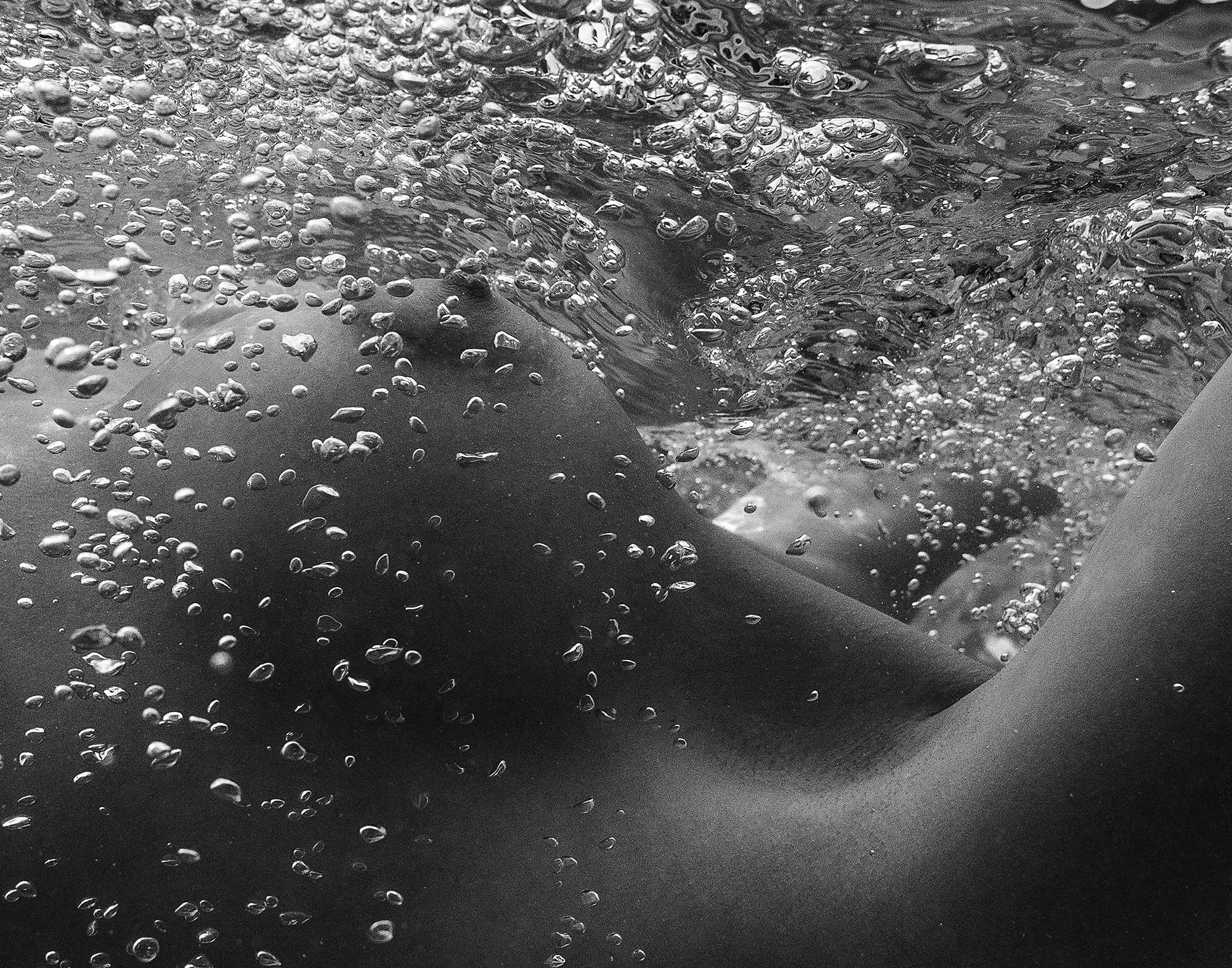 Photographie sous-marine en noir et blanc d'une belle jeune femme nue dont les seins sont recouverts de bulles d'air.

