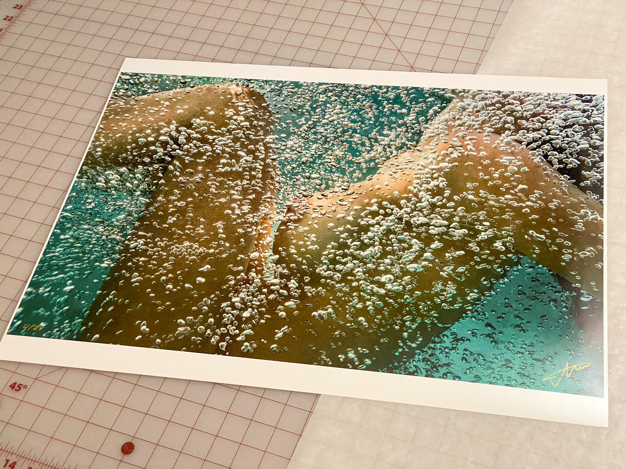 Une photo sous-marine d'une jeune femme nue enveloppée dans des bulles d'air. La photographie ne représente que son corps, le visage n'est pas visible. Une œuvre d'art très lumineuse qui attire l'œil. 

La piscine était glaciale. Après 15 minutes de