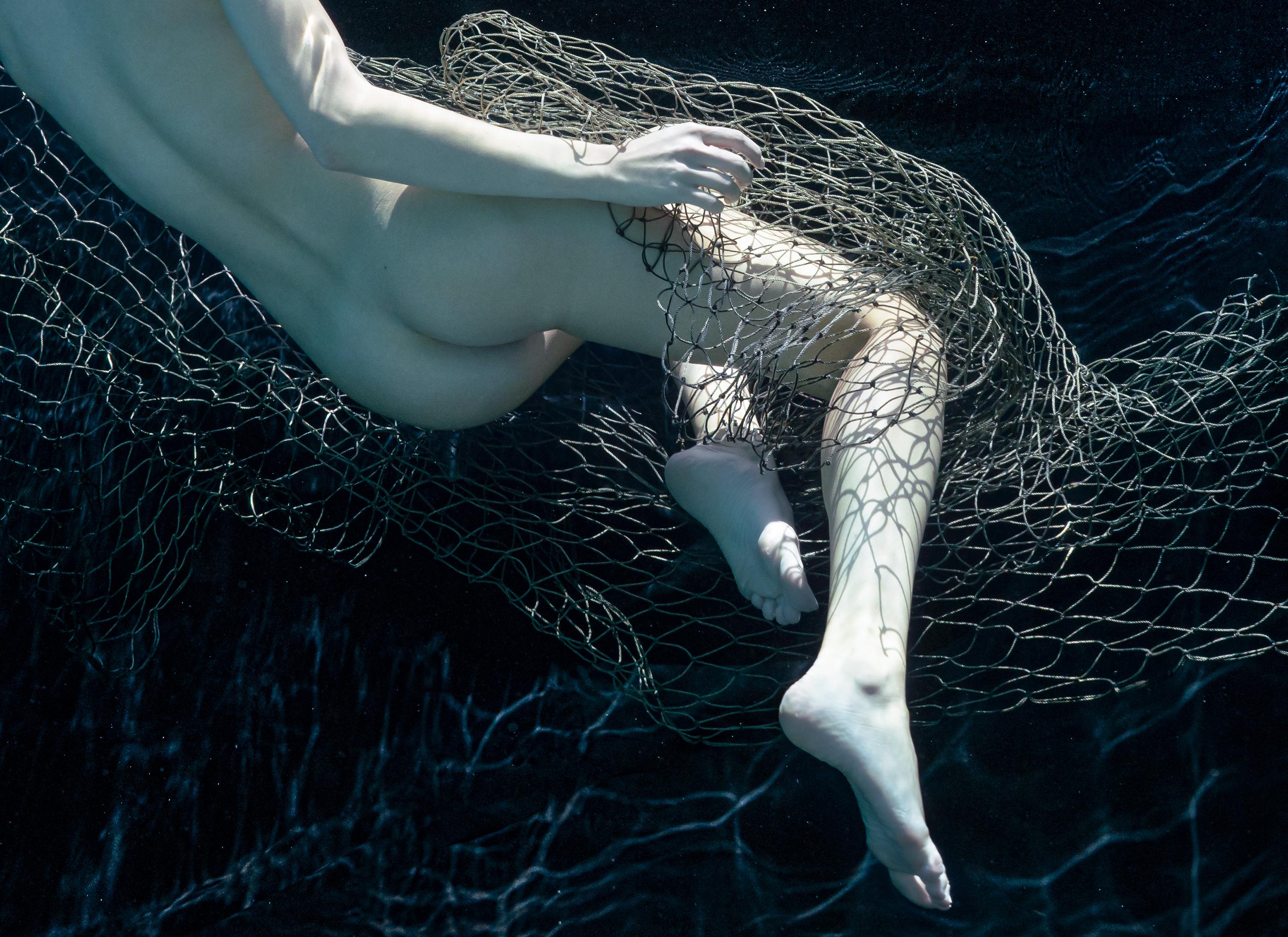 An underwater almost monochrome photograph of a naked young women wrapped in fishing net.

Original digital archival pigment print signed by the artist.
Limited edition of 24. 
Paper size: 25