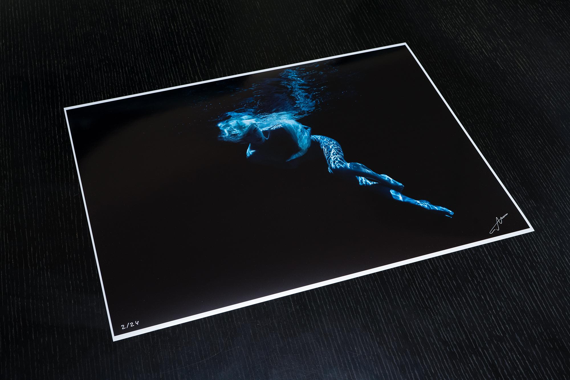 An underwater photograph of a nude model diving in blue light on a black background. 

Original gallery quality print signed by the artist. 
Digital archival pigment print on archival paper with metallic finish. 
Limited edition of 24
The artwork is