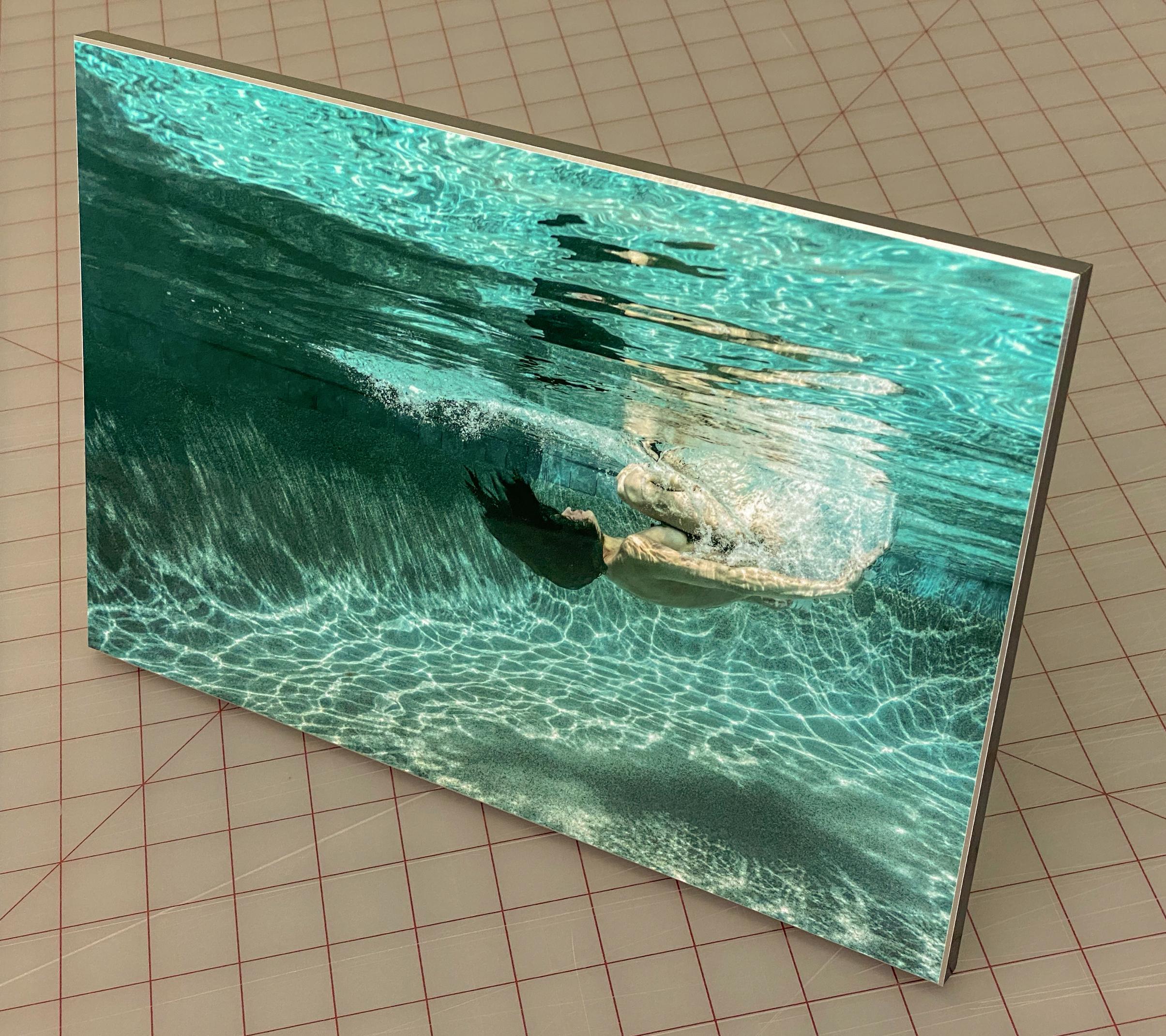 Unterwasseraufnahme einer nackten jungen Frau, die in einem Schwimmbecken taucht (rollt). Diese äußerst dynamische Fotografie ist reich an Grüntönen und sieht abstrakt aus, während sie in Wirklichkeit ganz figurativ ist.
Dieses Foto ist der erste