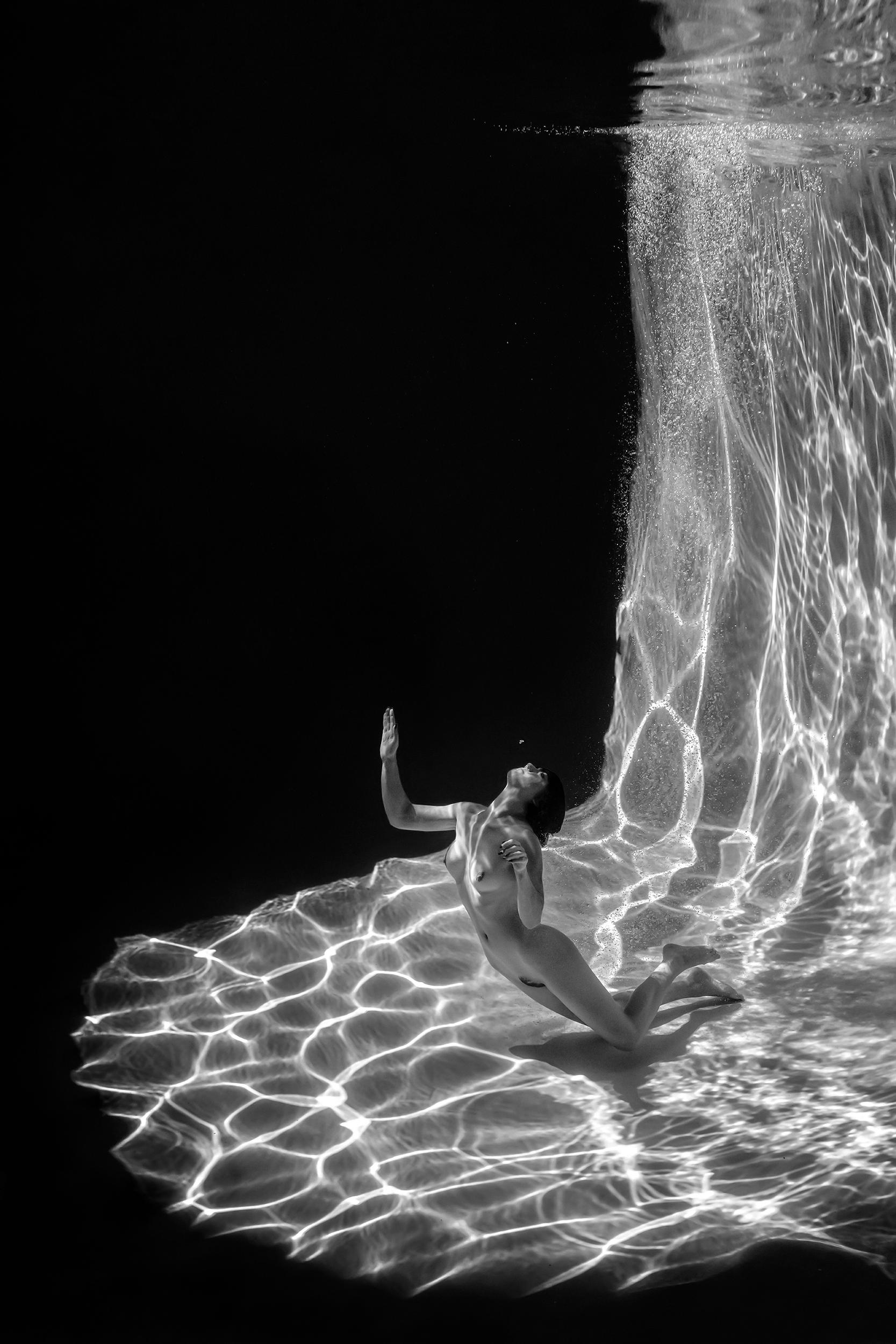 Marble Cave is a series of three underwater black and white photographs depicting a young naked woman swimming in a pool. Her strong body drops a bizarre shadow on the bottom of the pool covered with net of ripple shades and glares. 
This photograph