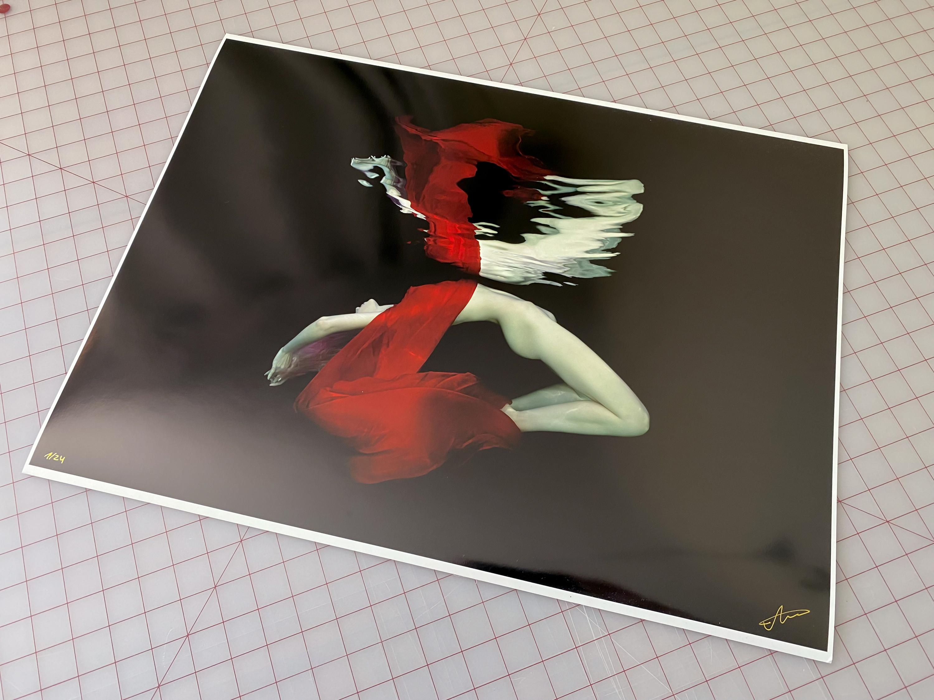 Ein Unterwasserfoto einer nackten jungen Frau, die teilweise in einen leuchtend roten Schal gehüllt ist - auf schwarzem Hintergrund.

Original-Pigmentdruck in Galeriequalität, vom Künstler signiert. 
Limitierte Auflage von 24 Stück
Das Kunstwerk ist