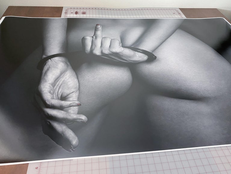 A black and white photograph of a perfect woman's buttocks and her handcuffed hands giving a finger.

Original gallery quality print signed by the artist. 
Digital archival pigment print. 
Paper size 44