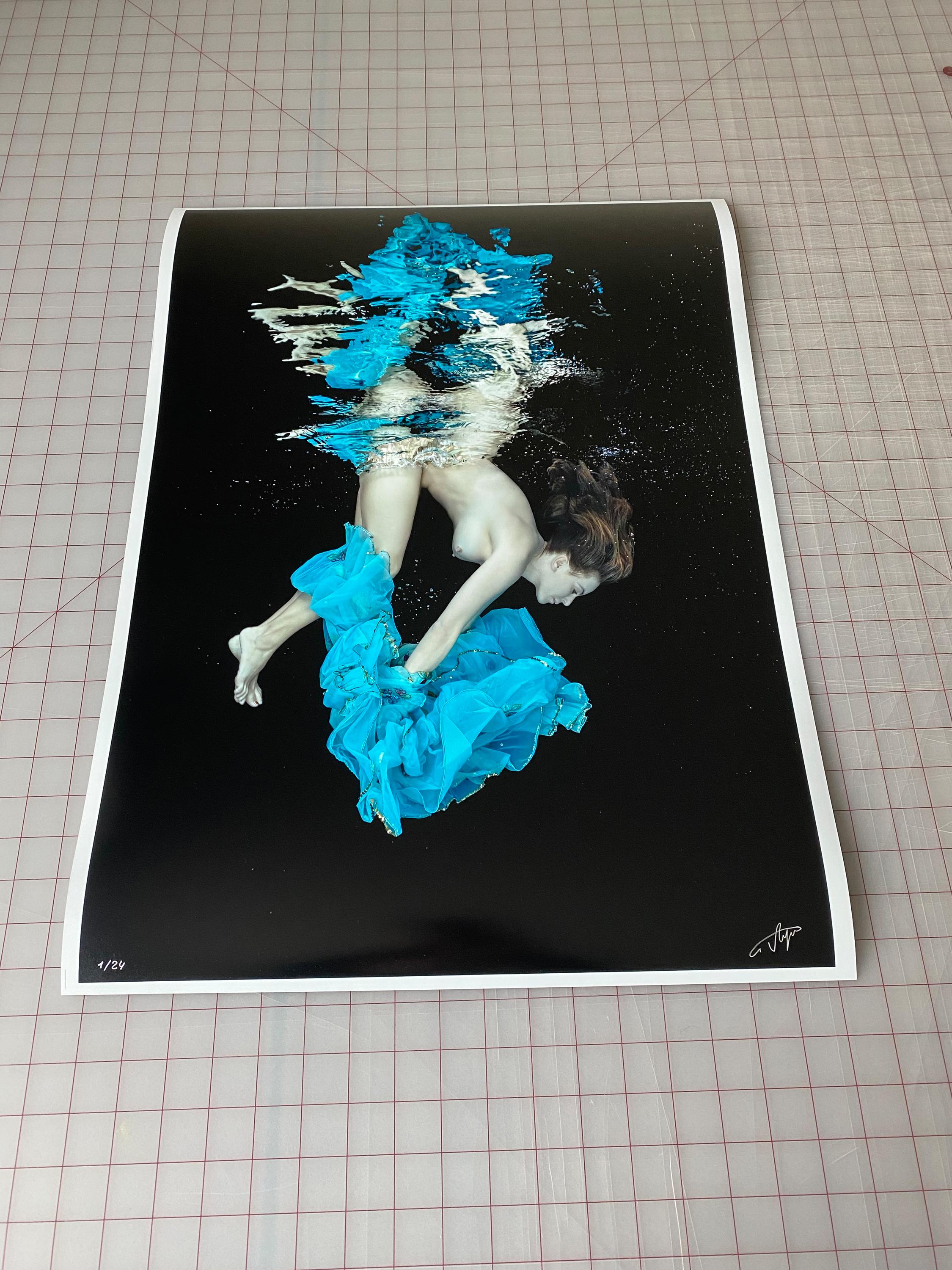An underwater photograph of a naked young women diving next to the bright turquoise dress she just took off. 

Original gallery quality print signed by the artist. 
Digital archival pigment print. 
Paper size 24