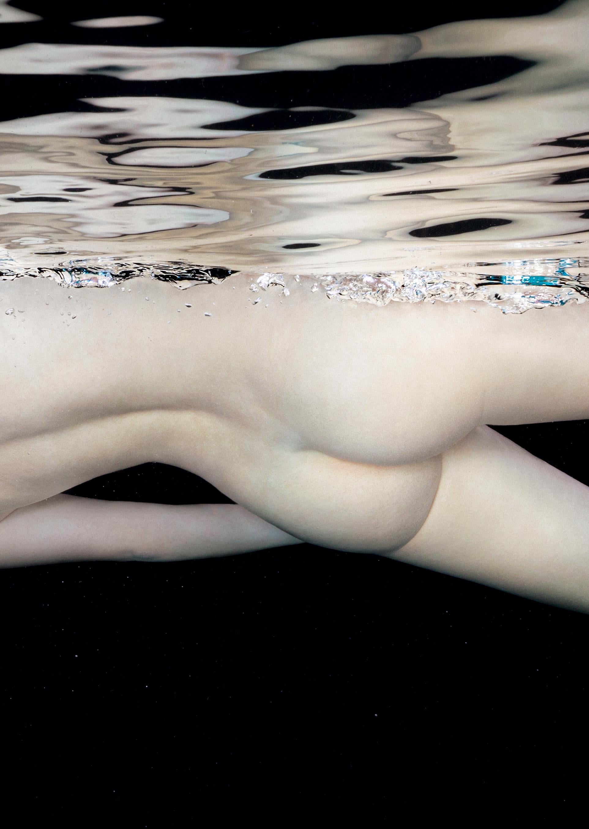 An underwater photograph of a naked young woman on neutral black background. This photograph belongs to the series Porcelain. The series includes my favorite photographs of nude models in the porcelain color scheme on the black background. The