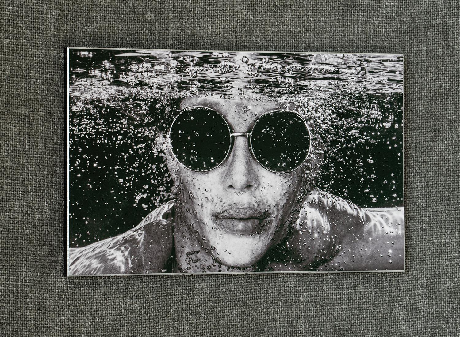 This striking monochromatic underwater fine art portrait captures celebrity Justin Jedlica in a moment of aquatic serenity. The high-contrast black and white treatment emphasizes the sculptural qualities of form, while countless air bubbles create a