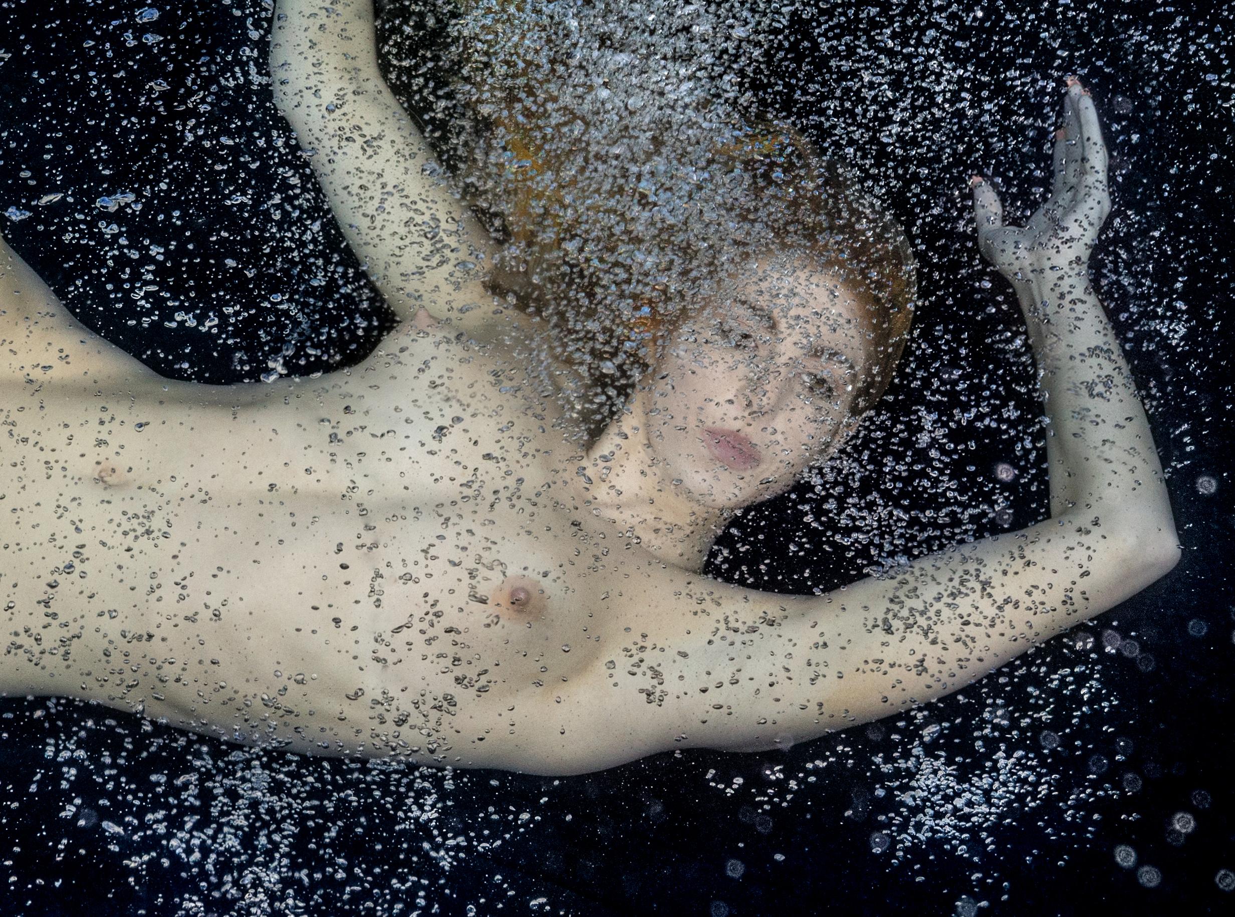 Unterwasseraufnahme einer jungen Frau mit goldenem Haar auf dem Grund eines Schwimmbeckens.  Ihr schöner nackter Körper ist in Wolken von Luftblasen gehüllt. 

Original-Pigmentdruck in Galeriequalität.  
Limitierte Auflage von 24 Drucken