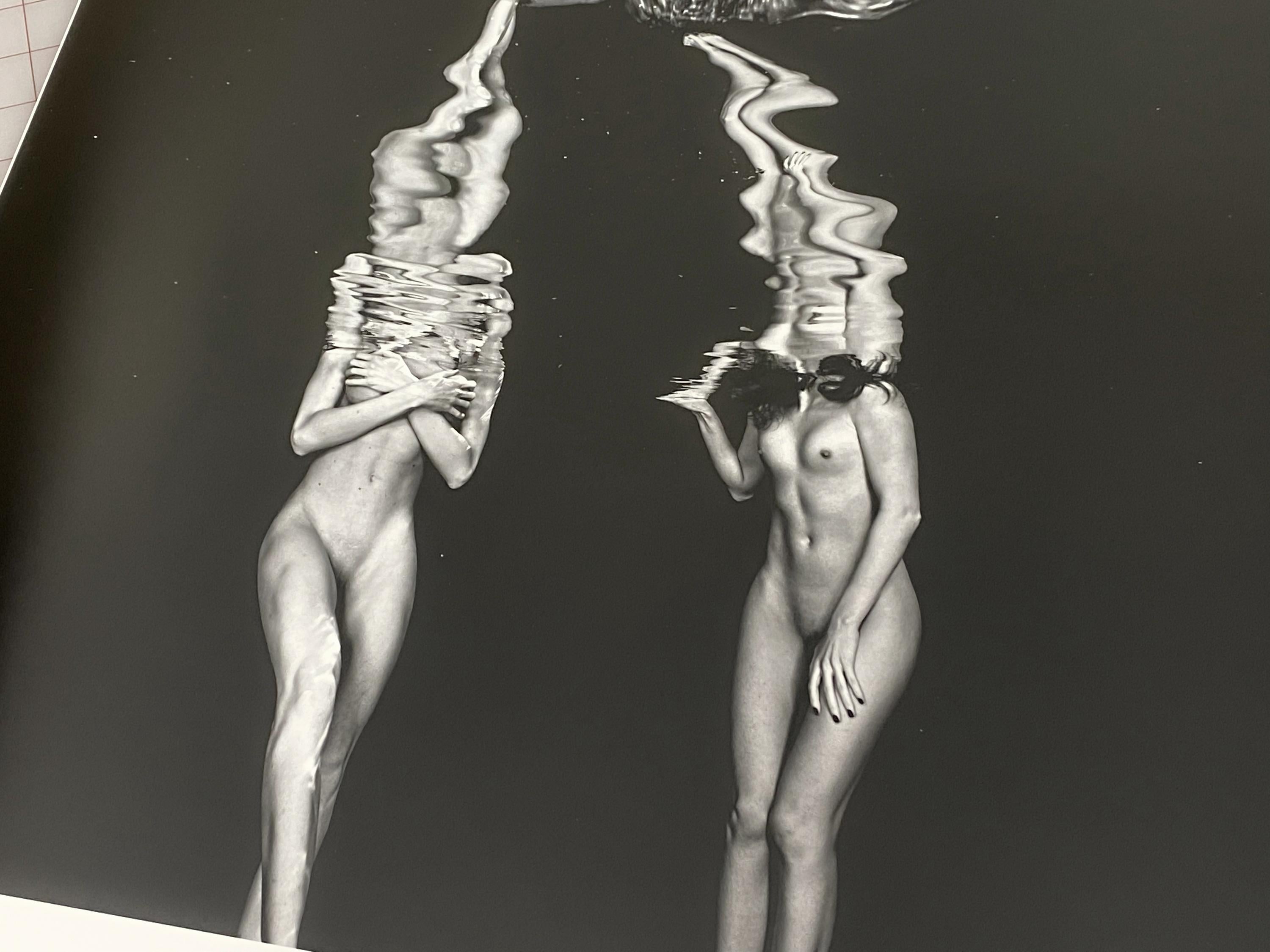 Eine Unterwasser-Schwarzweiß-Fotografie von zwei Frauen, die sich im Schwimmbad unterhalten, während ihre Köpfe über dem Wasser schweben. Die Köpfe sind durch schwarzes Wasser vor der Kamera verborgen.

Original-Pigmentdruck in Galeriequalität, vom