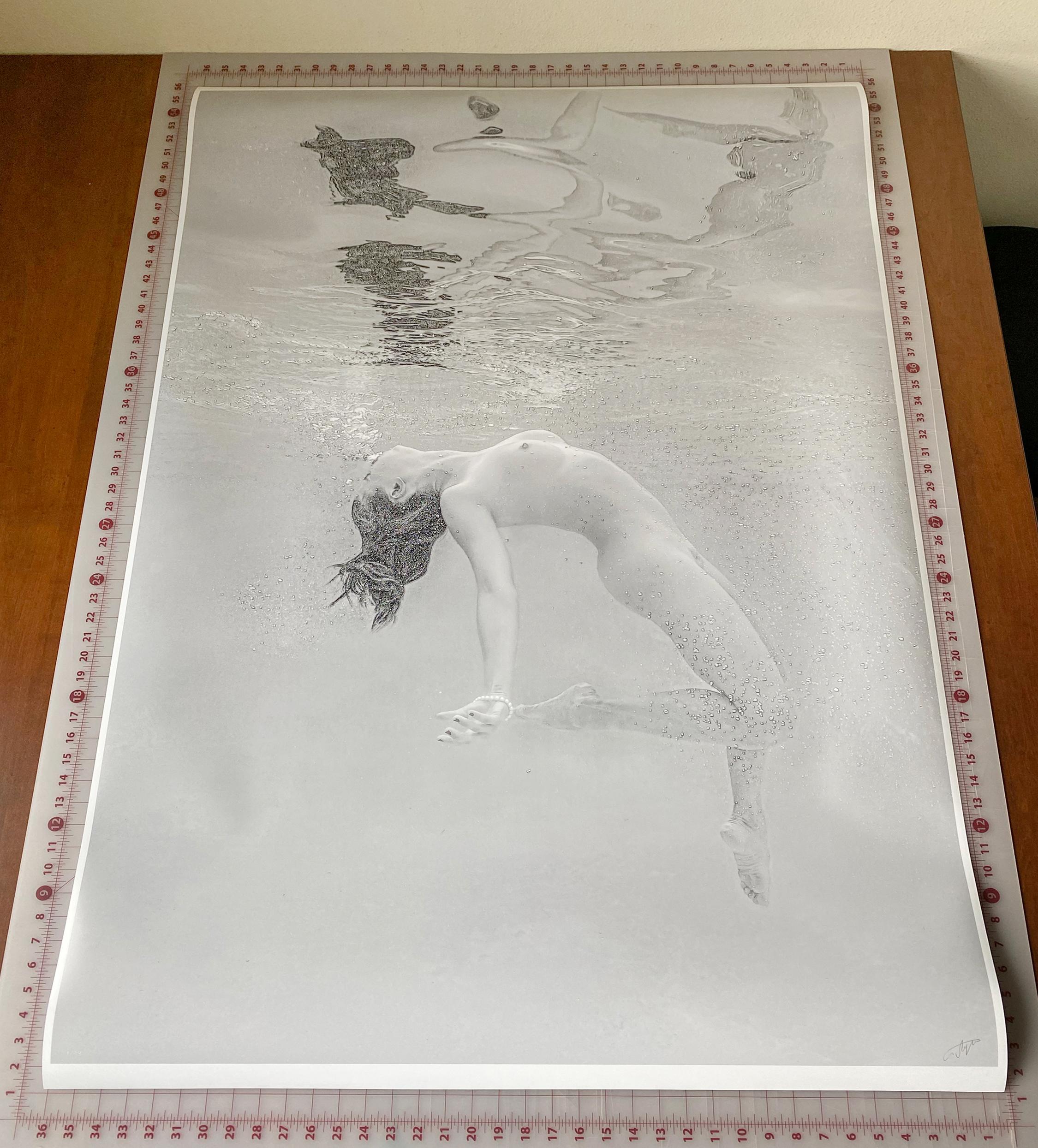 A black and white photograph of a naked young woman diving in a pool. The woman is coming from the depth up toward the surface and her body reflects in the internal water surface.

Original gallery quality archival pigment print signed by the