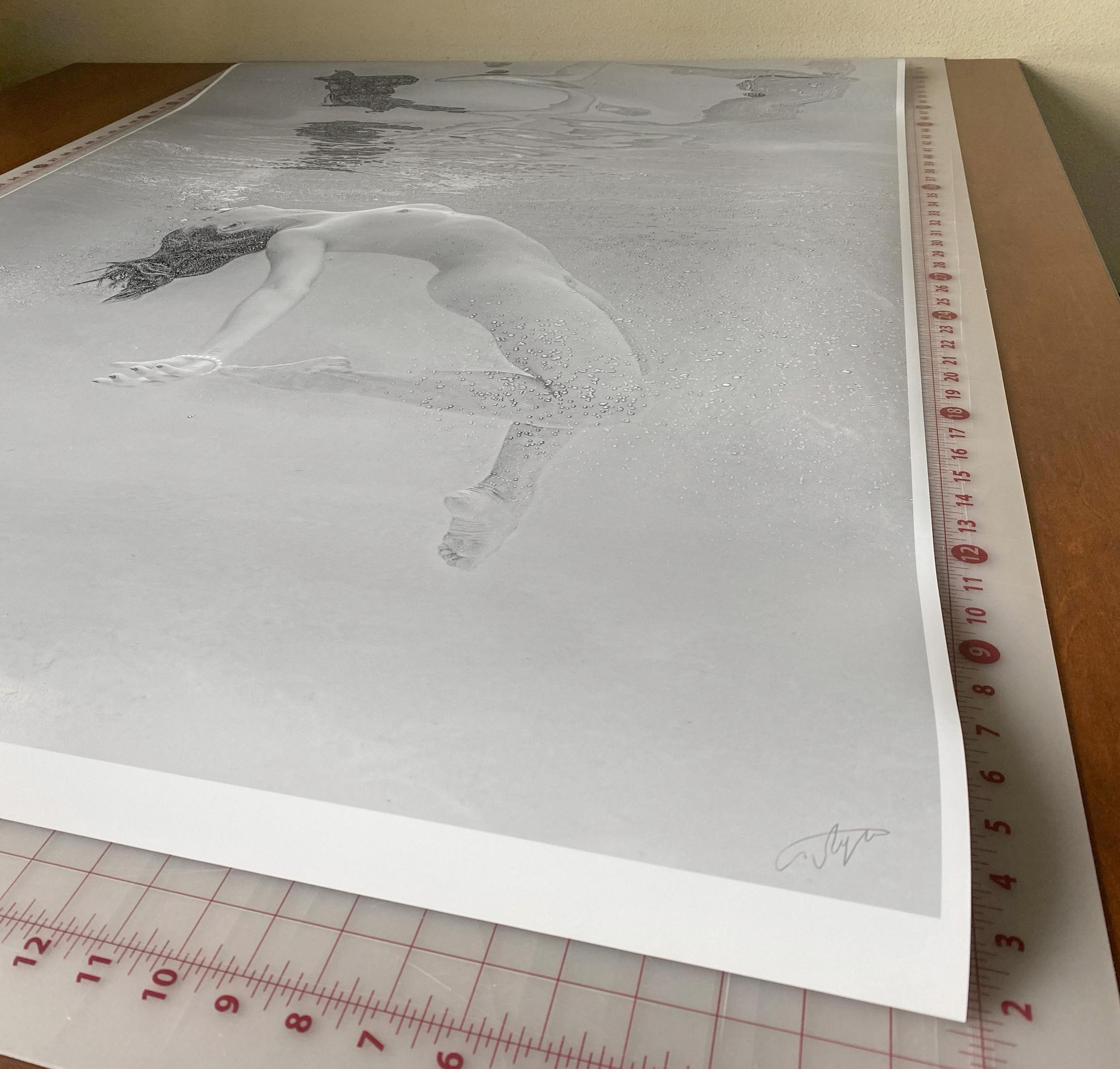 A black and white photograph of a naked young woman diving in a pool. The woman is coming from the depth up toward the surface and her body reflects in the internal water surface.

Original gallery quality archival pigment print signed by the